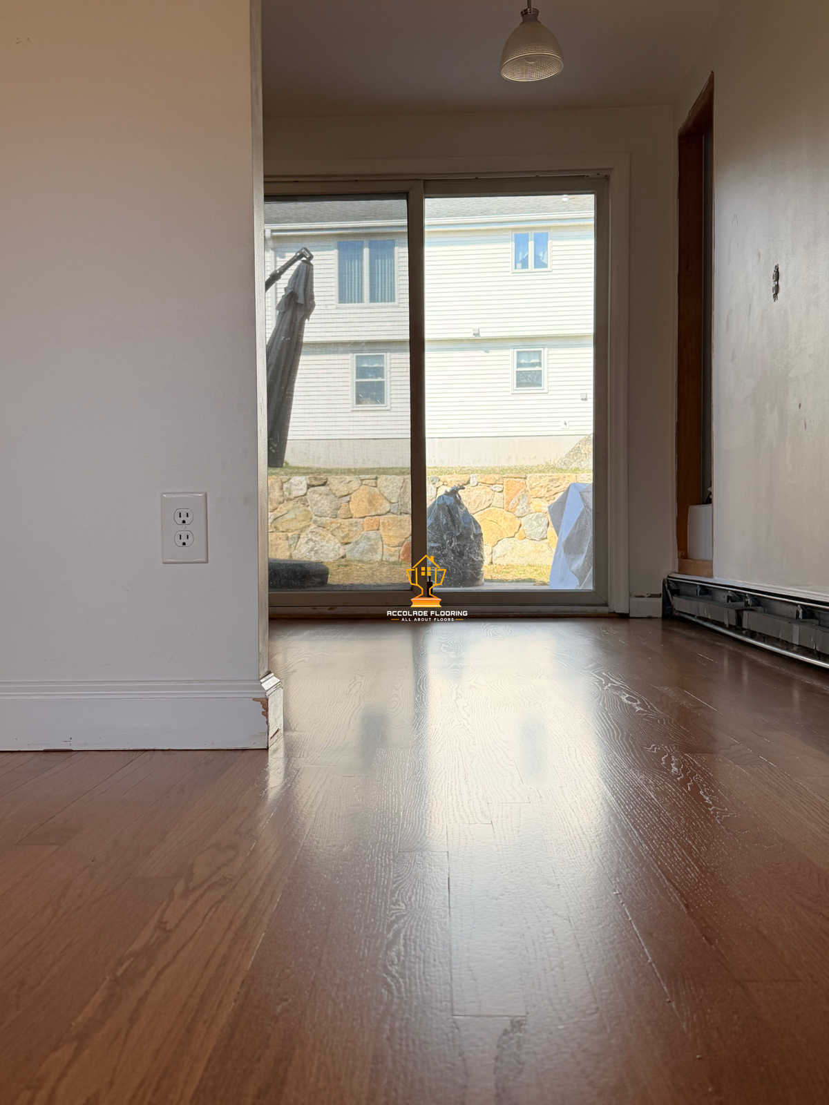 Empty room with a wooden floor, a sliding glass door leading outside, and a stone wall visible through the window.