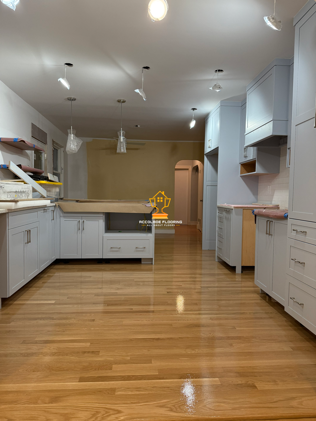 Kitchen under renovation with white cabinets, plywood countertops, hardwood floors, and unfinished ceiling lights.