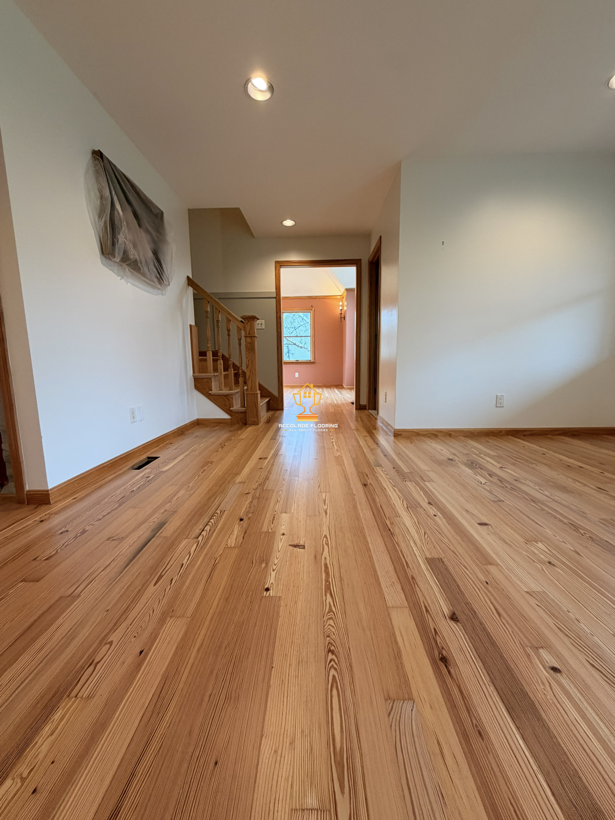 Empty living room with wooden floors, staircase, and doorways leading to other rooms, during daytime.