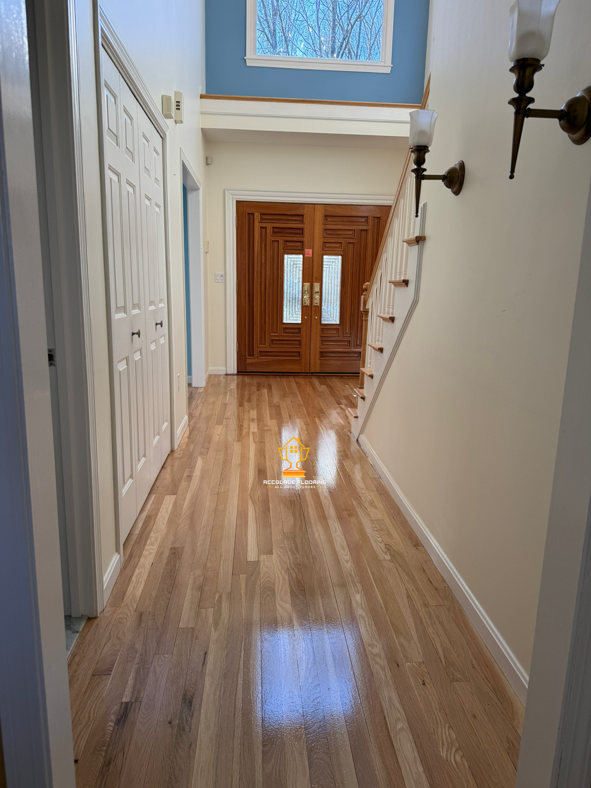 Entryway with wooden front door, staircase on the right, white walls, wood flooring, and light fixtures on the wall.