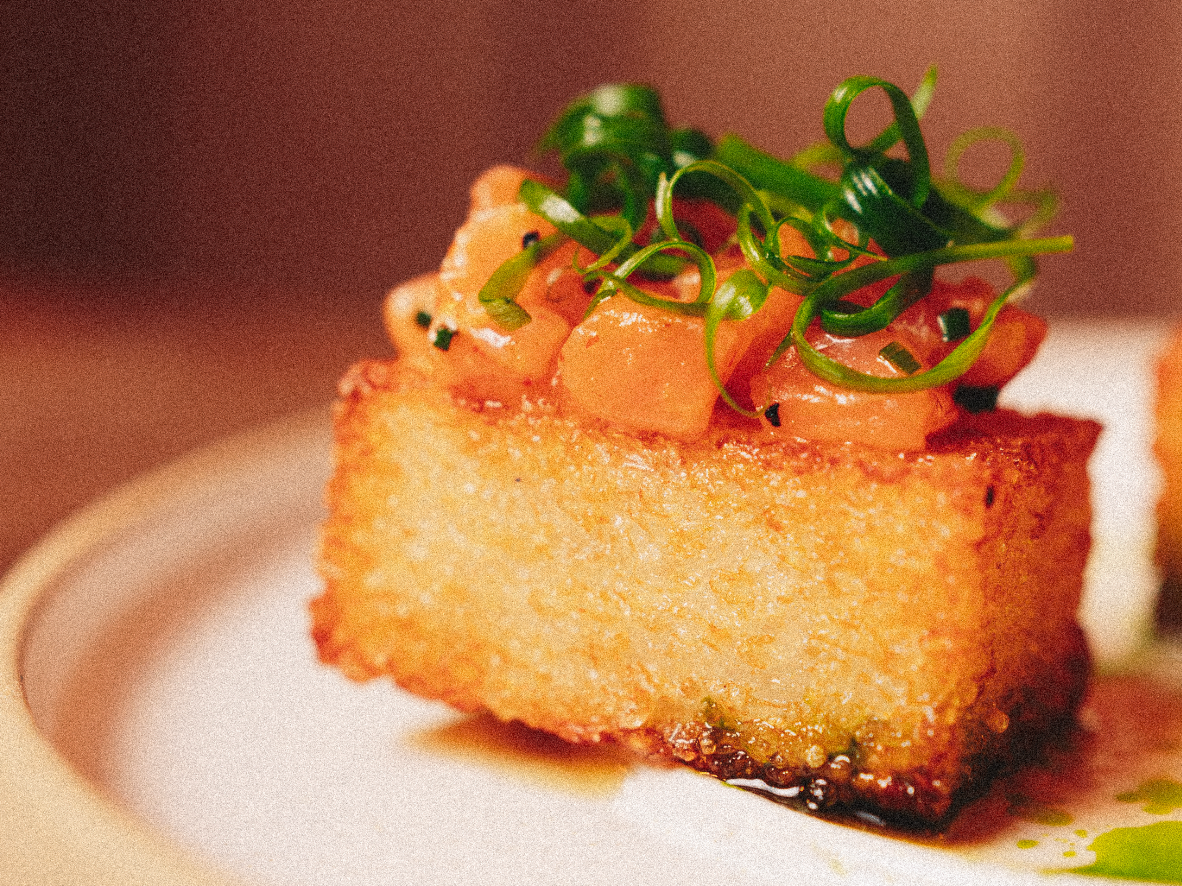 Close-up of a piece of fried tofu topped with chopped green onions and small diced tomatoes on a white plate. Served at Vera Restaurant Glasgow Southside 138 Nithsdale Road.