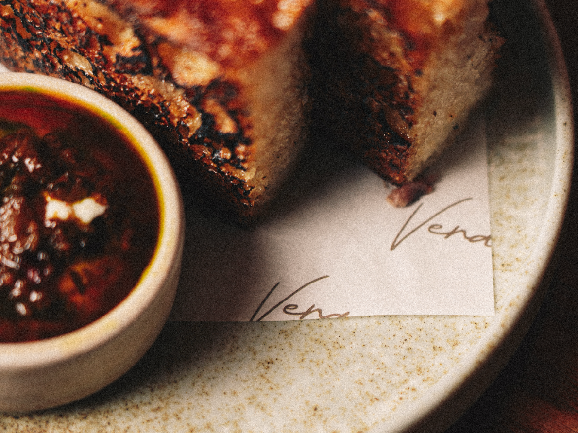 Close-up of a toasted sandwich with grill marks and a small bowl of dipping sauce or salsa on a plate with a paper underneath. Served at Vera Restaurant Glasgow Southside 138 Nithsdale Road.