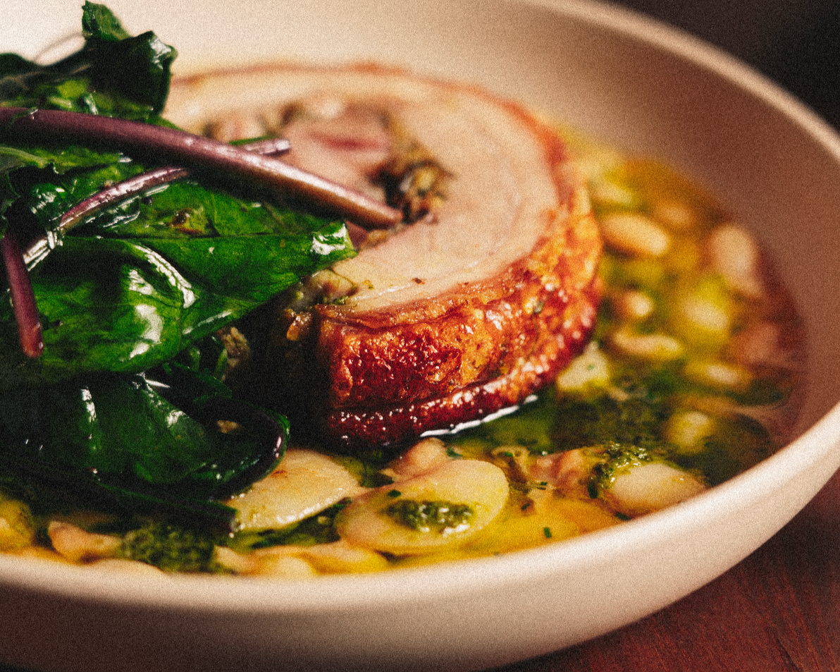 Close-up of a baked meat roulade on a bed of greens and white beans in a white bowl. Served at Vera Restaurant Glasgow Southside 138 Nithsdale Road.