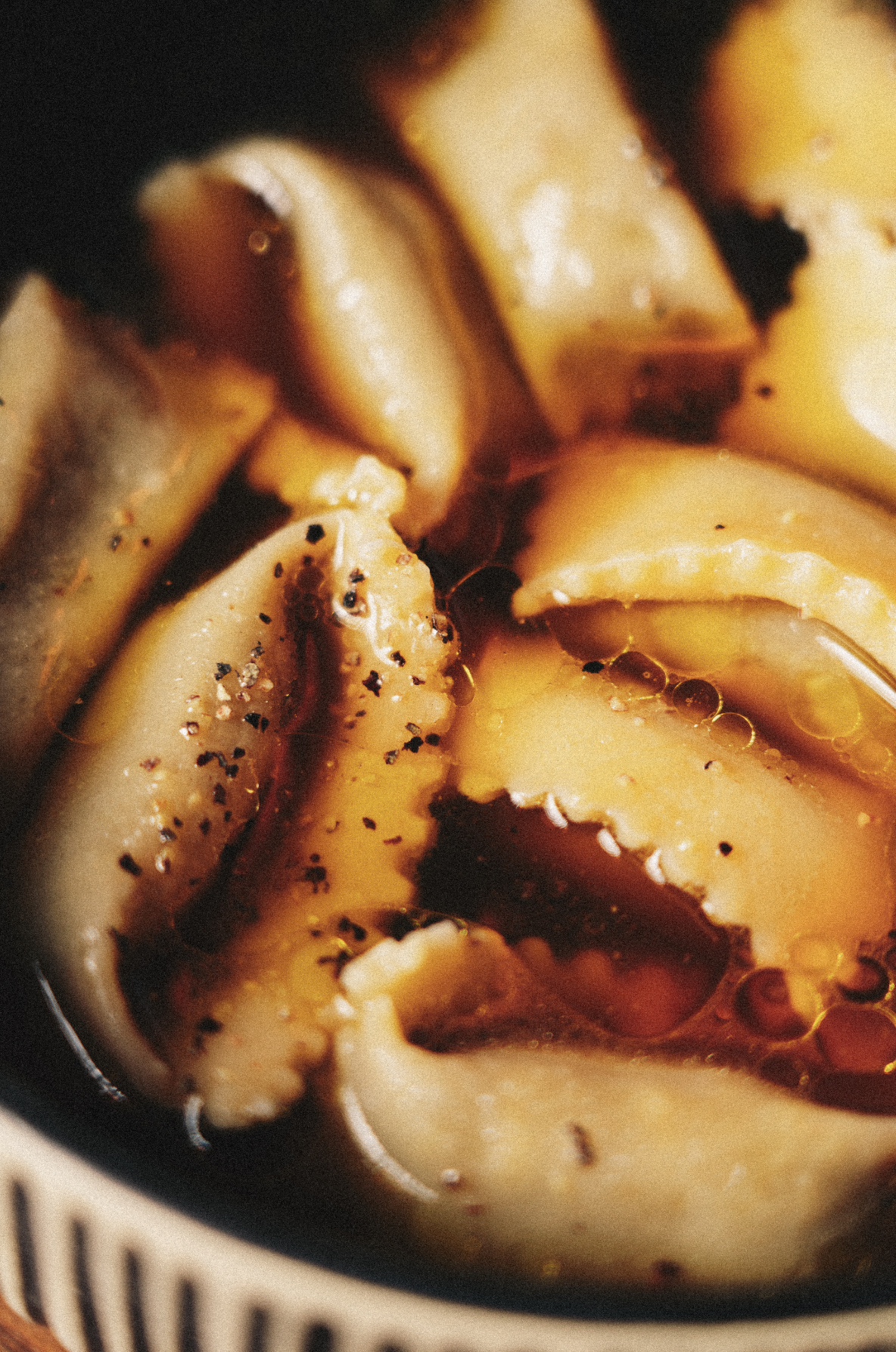 Close-up of sliced potatoes with black pepper, salt, and oil or butter, garnished with a sauce or gravy. Served at Vera Restaurant Glasgow Southside 138 Nithsdale Road.