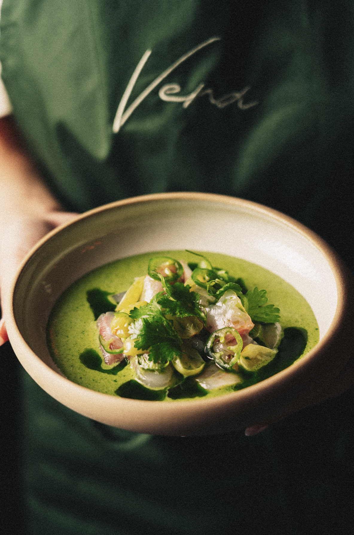 A bowl of green soup topped with sliced jalapeños, cilantro, and pieces of fish or seafood, garnished with herbs. Served at Vera Restaurant Glasgow Southside 138 Nithsdale Road.