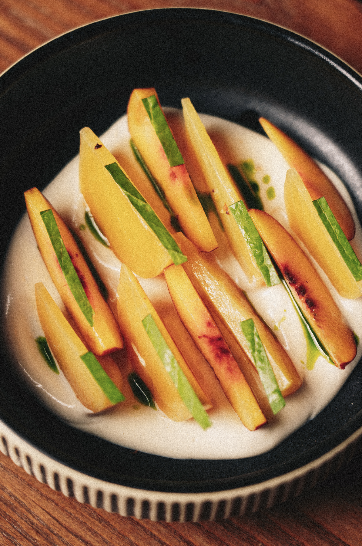 Slices of peach and cucumber arranged on a white plate with a creamy dip, inside a black ceramic bowl. Served at Vera Restaurant Glasgow Southside 138 Nithsdale Road.