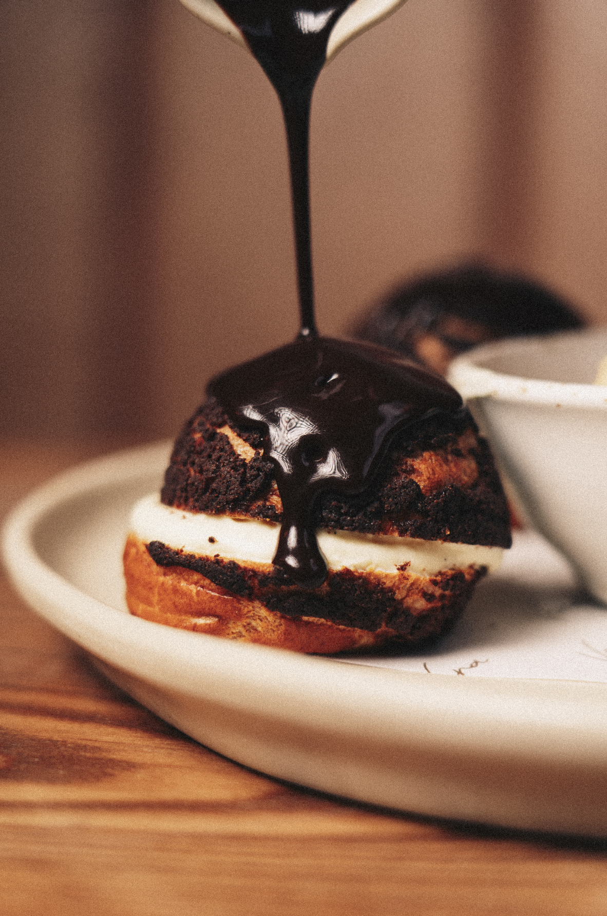 A chocolate and vanilla ice cream sandwich with chocolate syrup being poured over it, served on a white plate. Served at Vera Restaurant Glasgow Southside 138 Nithsdale Road.