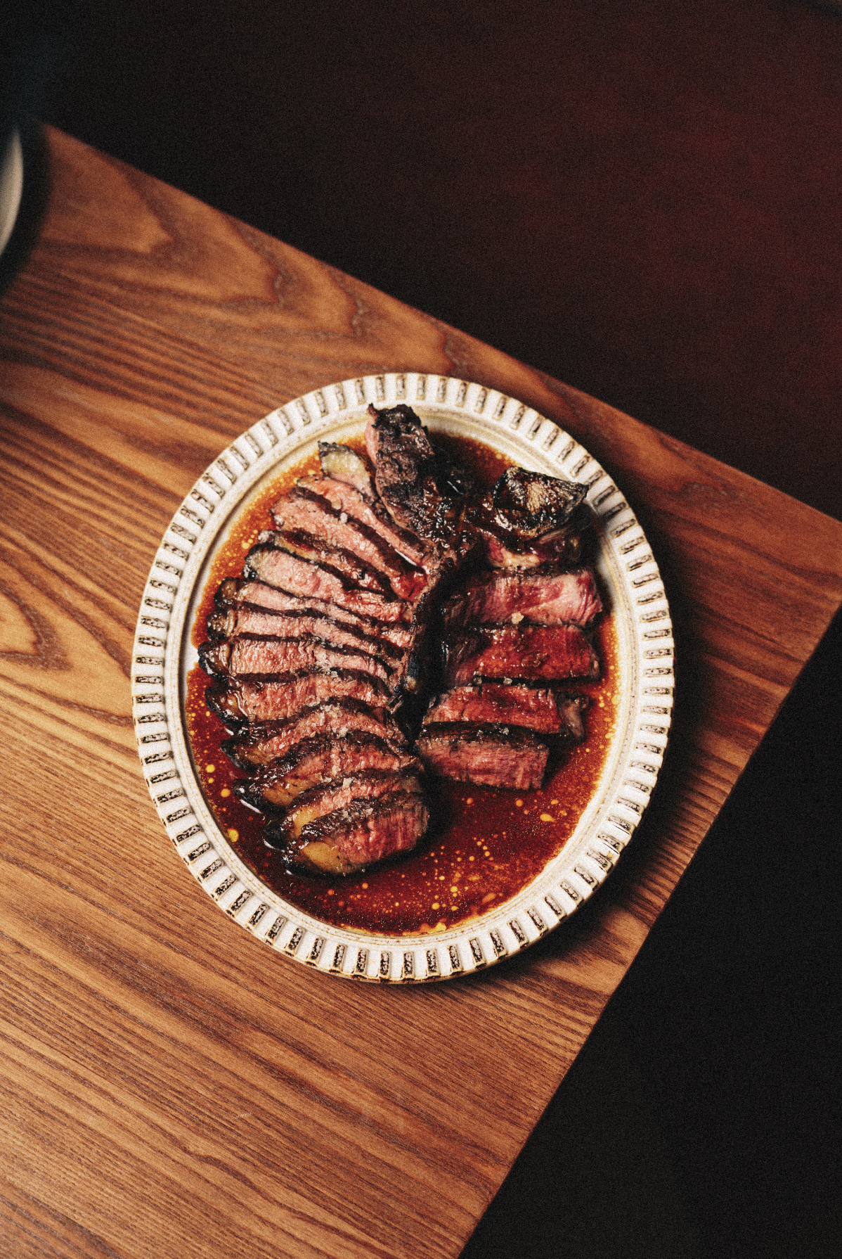 Sliced medium-rare steak with a dark sauce on a decorative oval plate placed on a wooden table. Served at Vera Restaurant Glasgow Southside 138 Nithsdale Road.