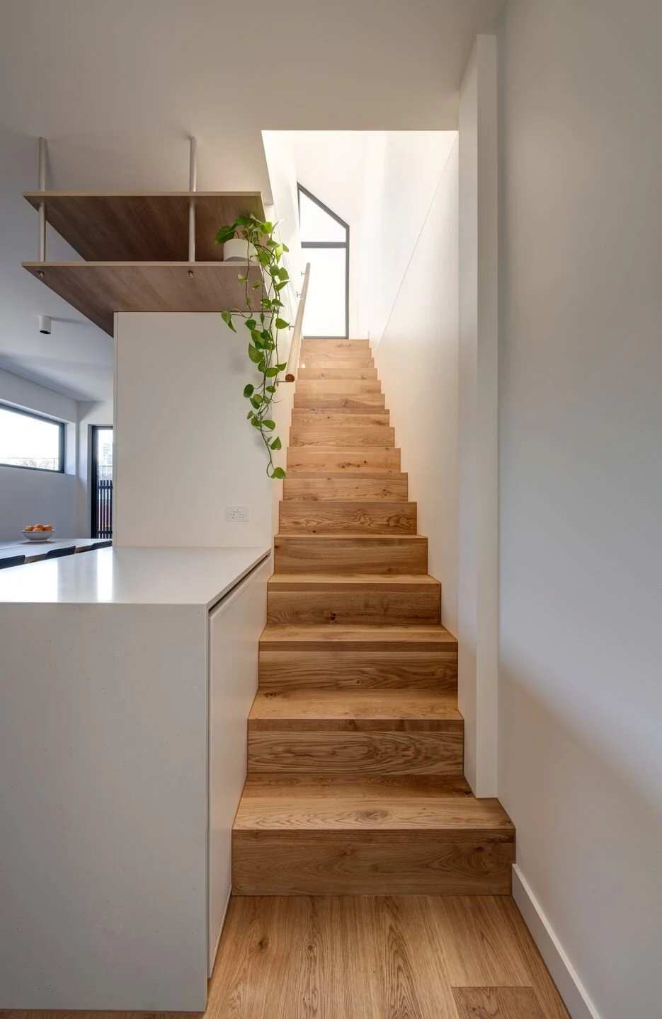 Wooden staircase leading up to a skylight window in a modern, minimalist interior.
