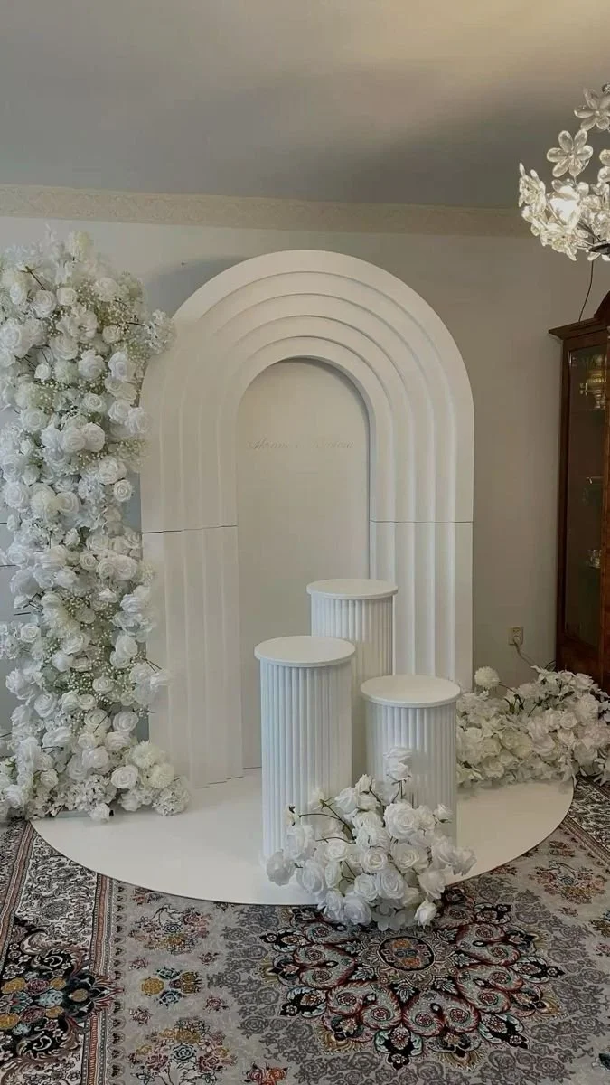 Wedding backdrop with white flower arrangements, white construction columns, and a white arched backdrop.