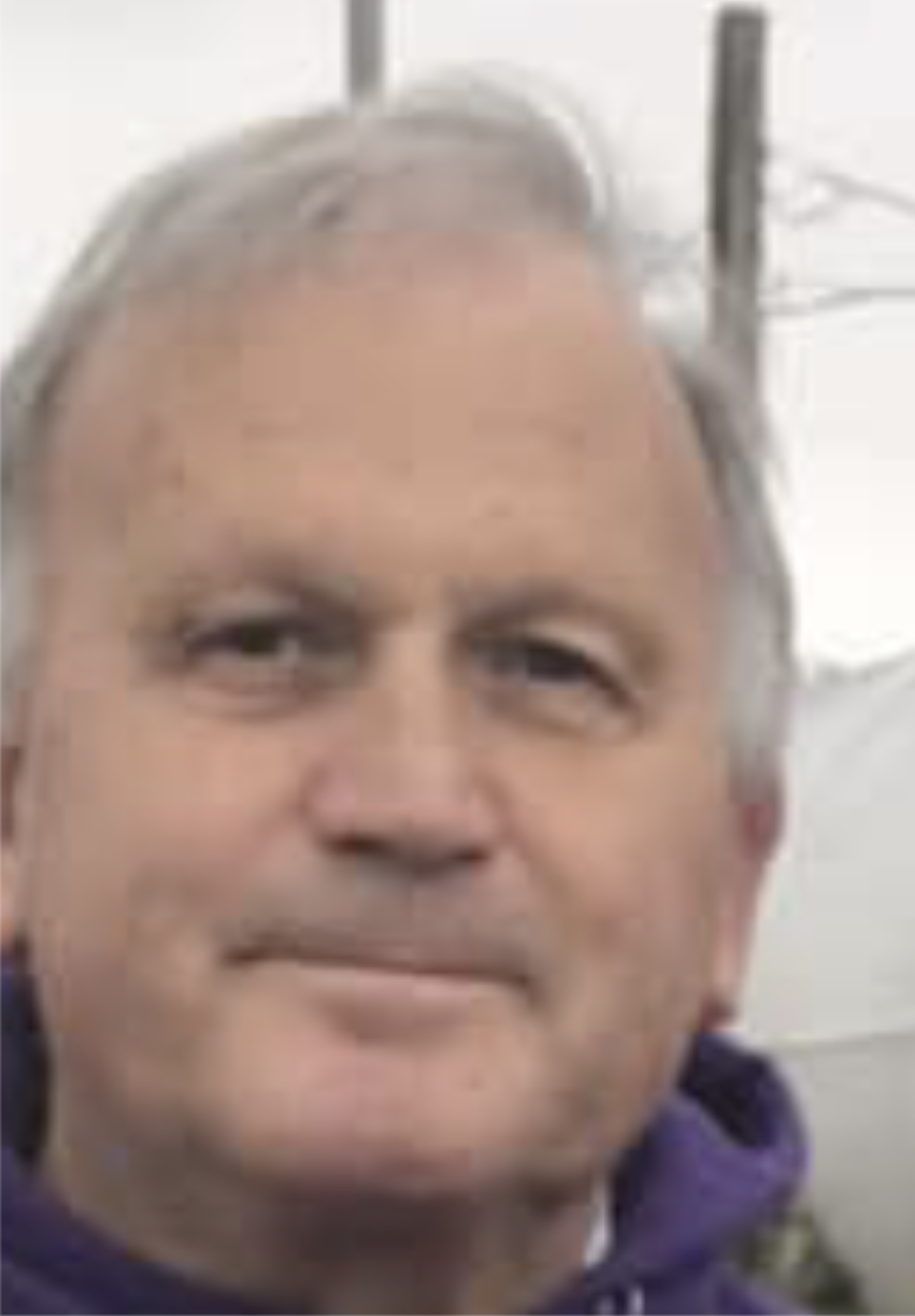 Close-up of a middle-aged man with short gray hair, light skin, and a slight smile, wearing a dark-colored jacket.