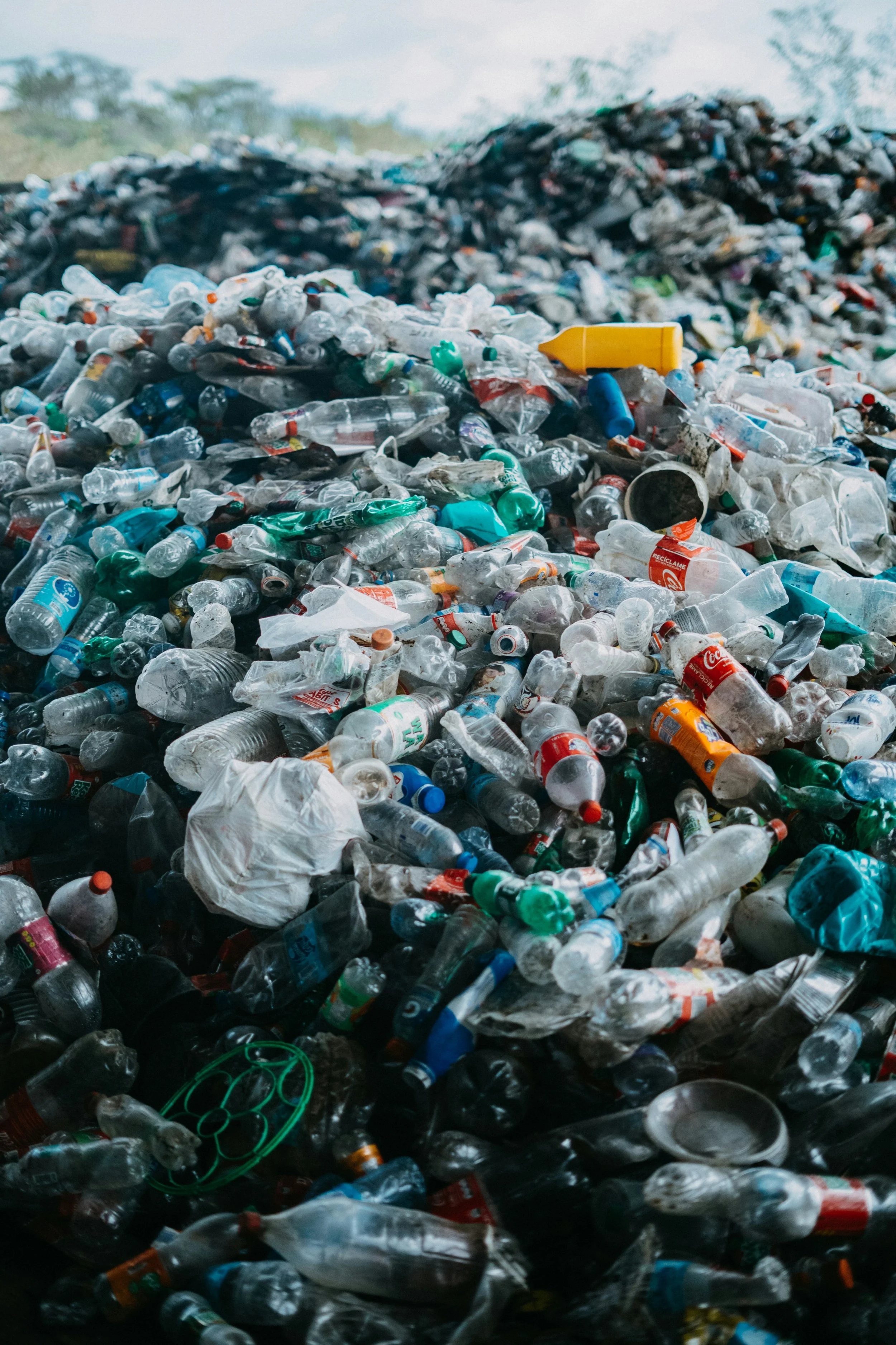 A large pile of discarded plastic bottles and trash in an open outdoor area.