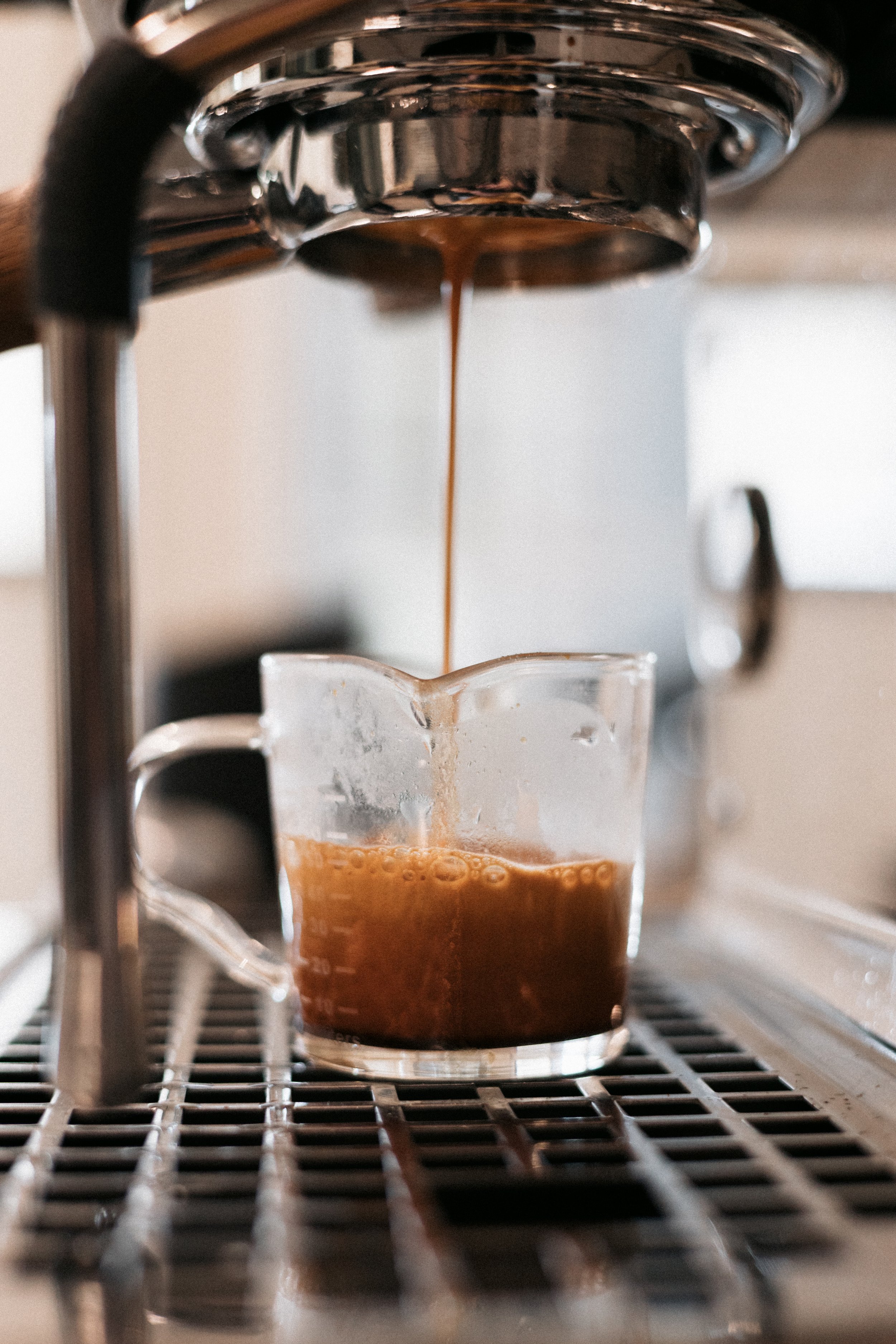 Close-up of espresso being brewed from a coffee machine, pouring into a clear glass cup placed on a metal grate.