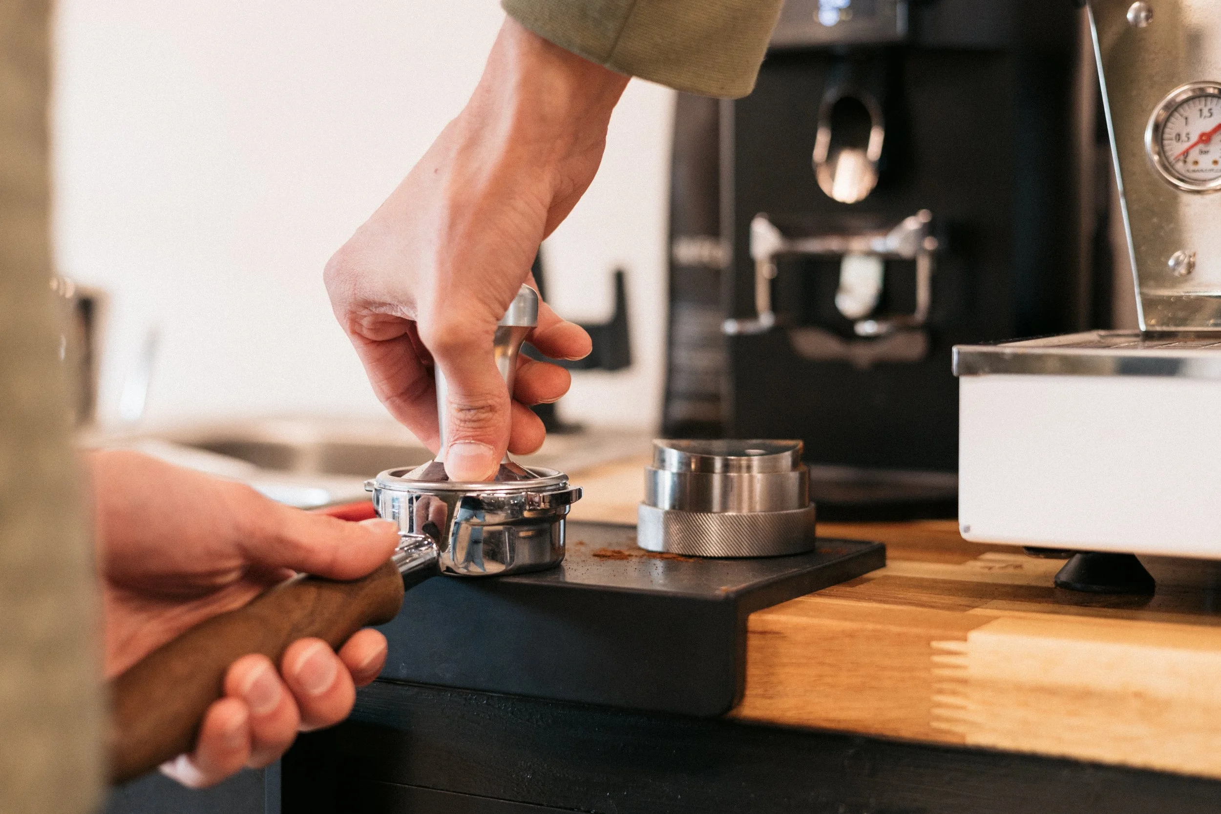 Person's hand using a tamper to press ground coffee into a portafilter for espresso on a kitchen countertop.