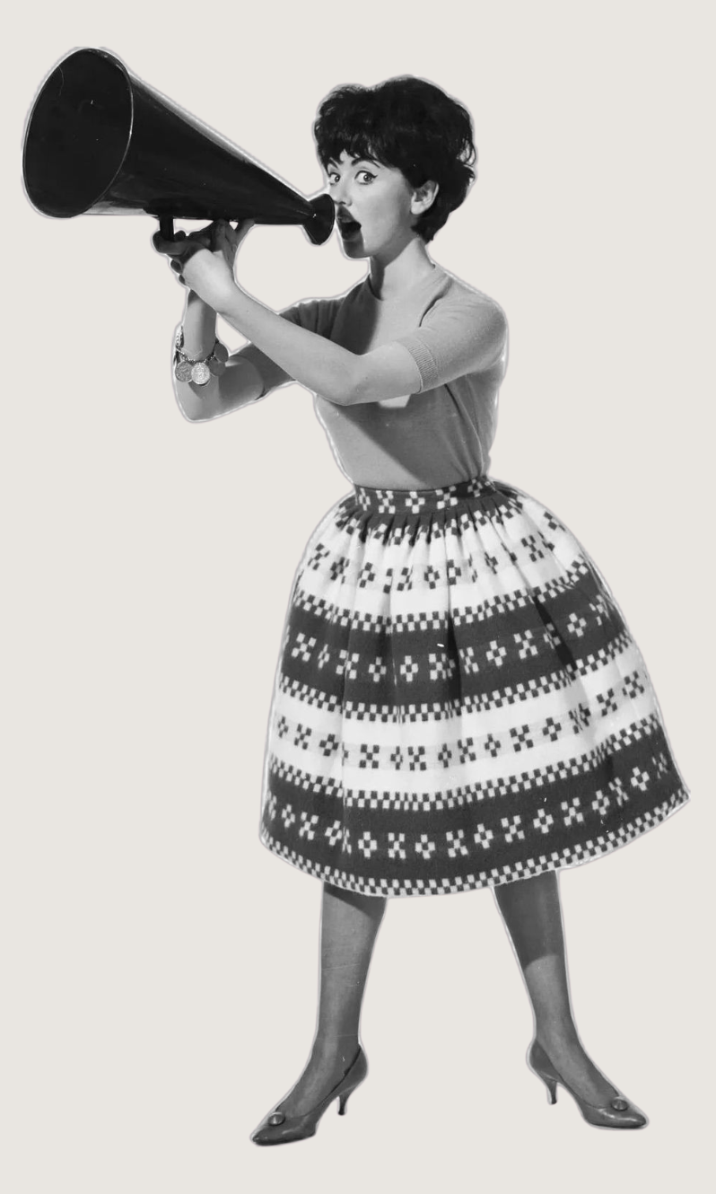 A vintage black and white photo of a woman holding a megaphone and speaking through it. She wears a patterned skirt, a fitted top, and high heels.