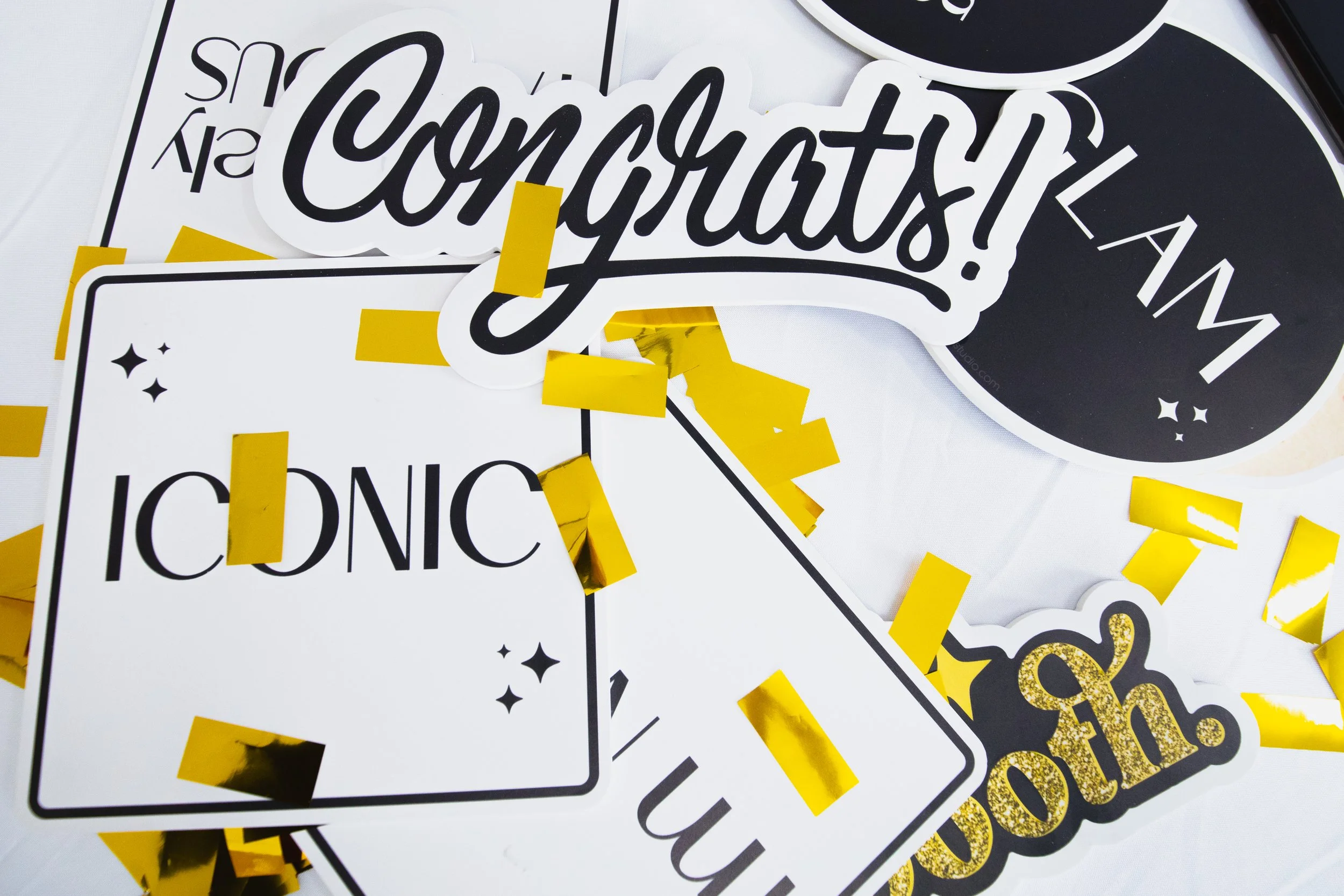 A collection of black and white signs with words such as 'Congratulations,' 'ICONIC,' and others, decorated with yellow rectangular confetti and small star shapes.