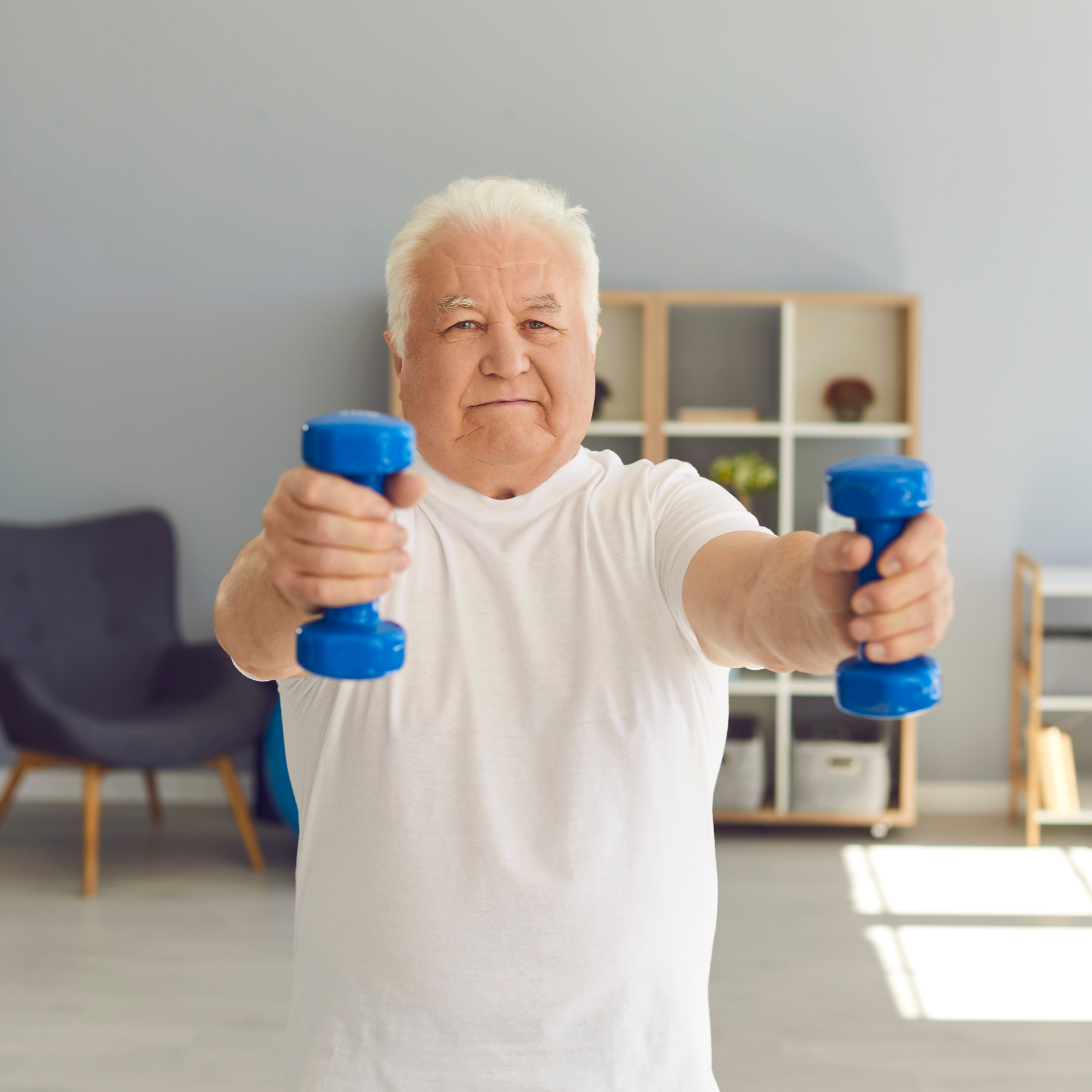 A woman in a wheelchair holding a dumbbell and smiling at a man kneeling beside her, giving her a high five in a living room.