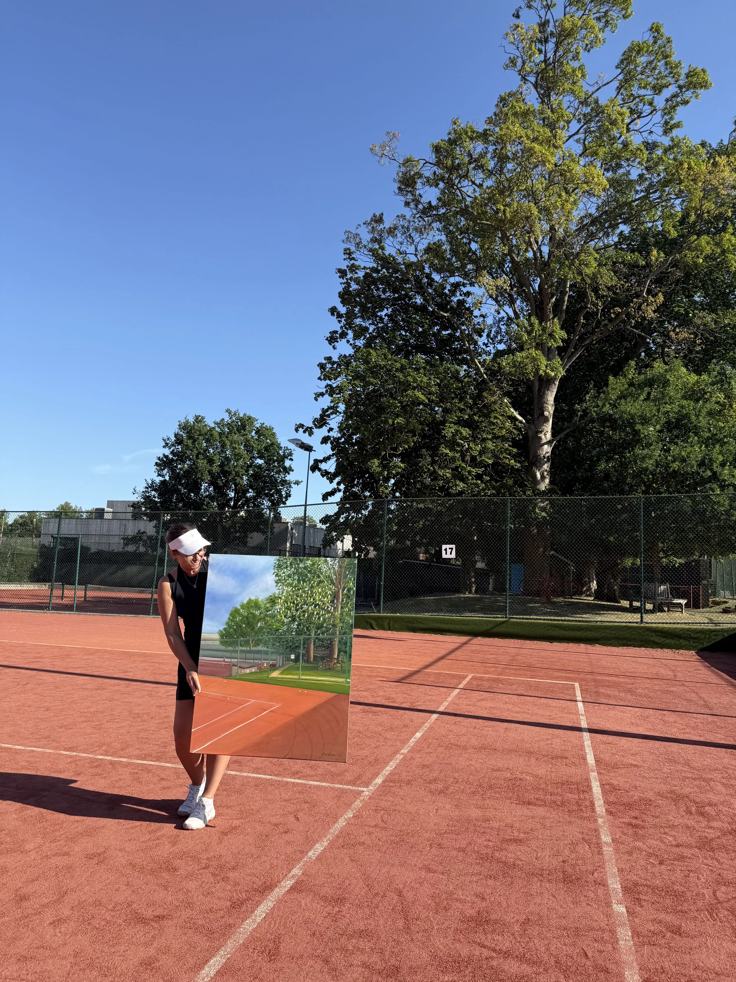 Maria Raskina holding her original oil painting, Court 17 in May, on Court 17 of Harpenden Lawn Tennis Club