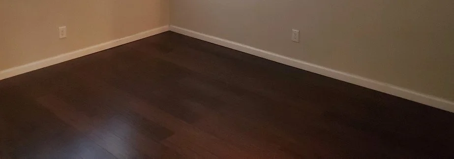 Installation of new dark hardwood flooring, and white baseboards.