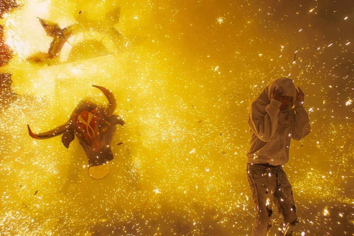 A fire bull erupts in sparks beside a man shielding his head, from Toros de Fuego by Gustavo Martínez Contreras