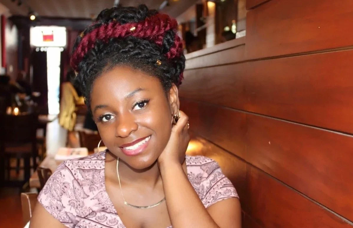 A young woman with red and black hairstyle, smiling, sitting in a restaurant.