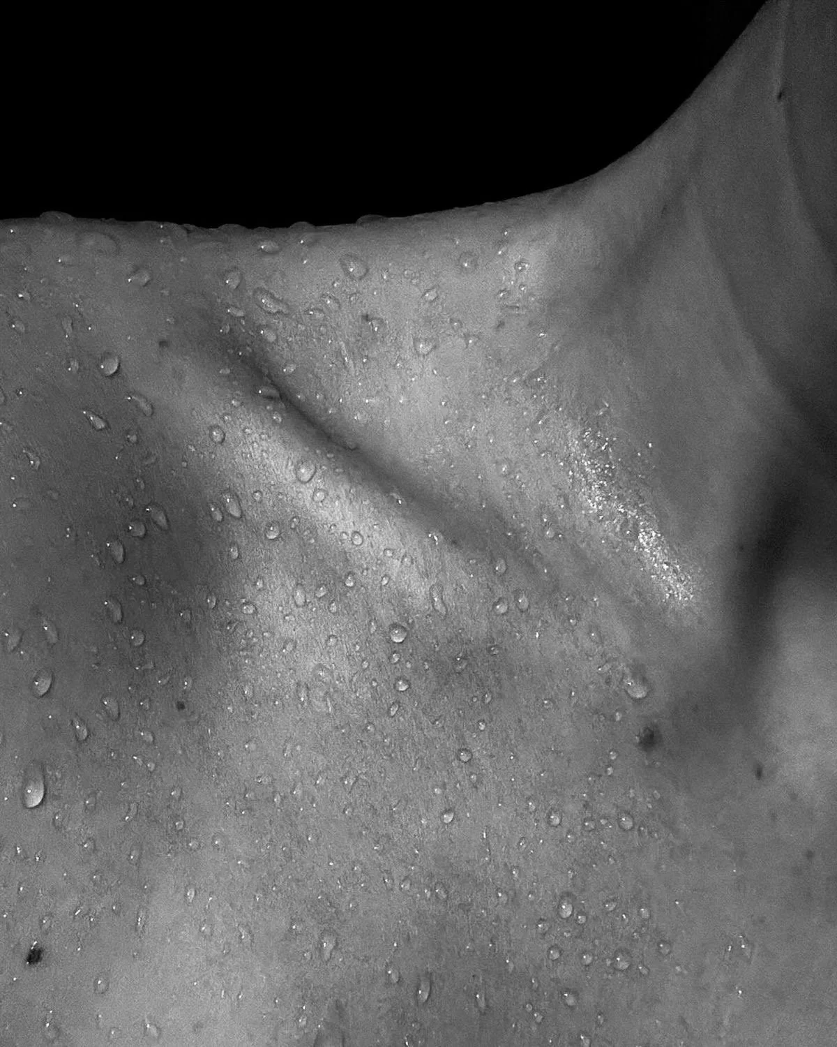 Close-up of a human face with water droplets, showing the cheek, nose, and part of the lips in black and white.