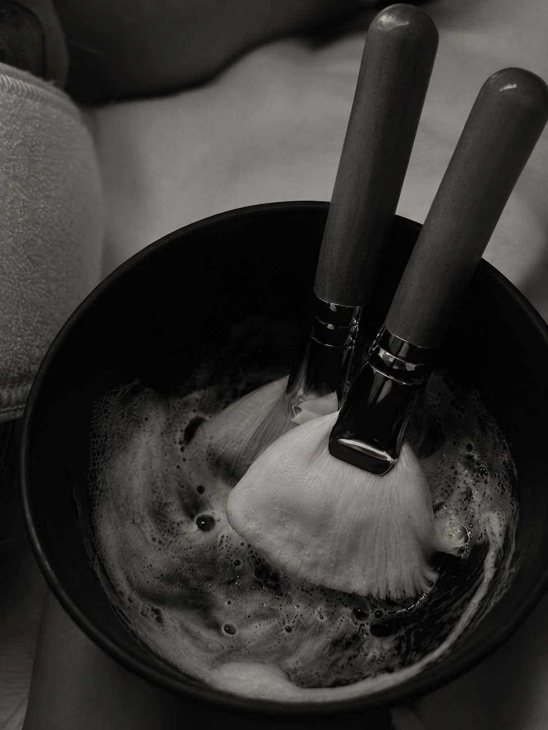 Two cake knives are inserted into a frosted bundt cake in a black bowl with bubbles visible in the frosting.