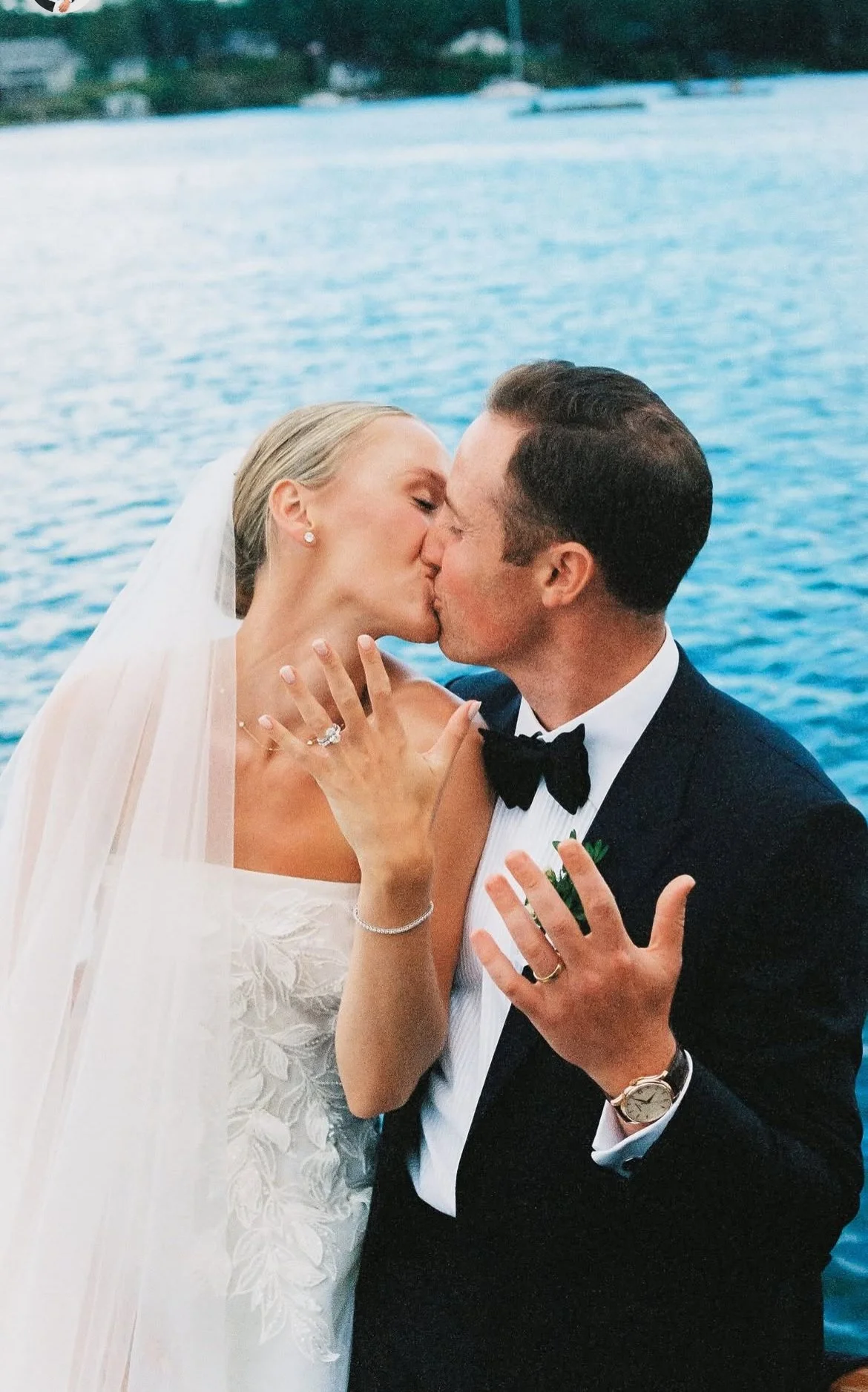 Bride and groom sharing a kiss by the water, with the bride wearing an elegant wedding dress and veil, and the groom in a tuxedo.