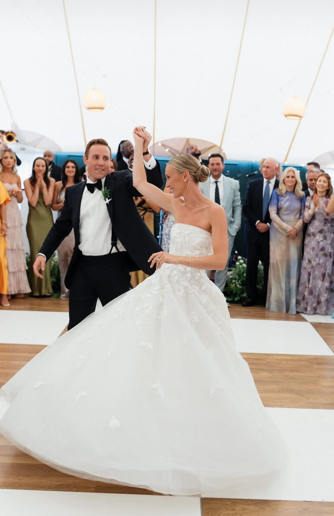 A bride and groom dancing at their wedding reception with guests watching in the background.