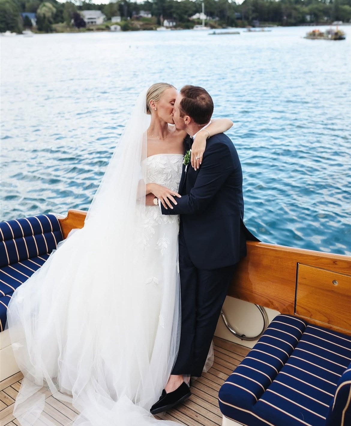 A newlywed couple sharing a kiss on a boat with water and boats in the background.