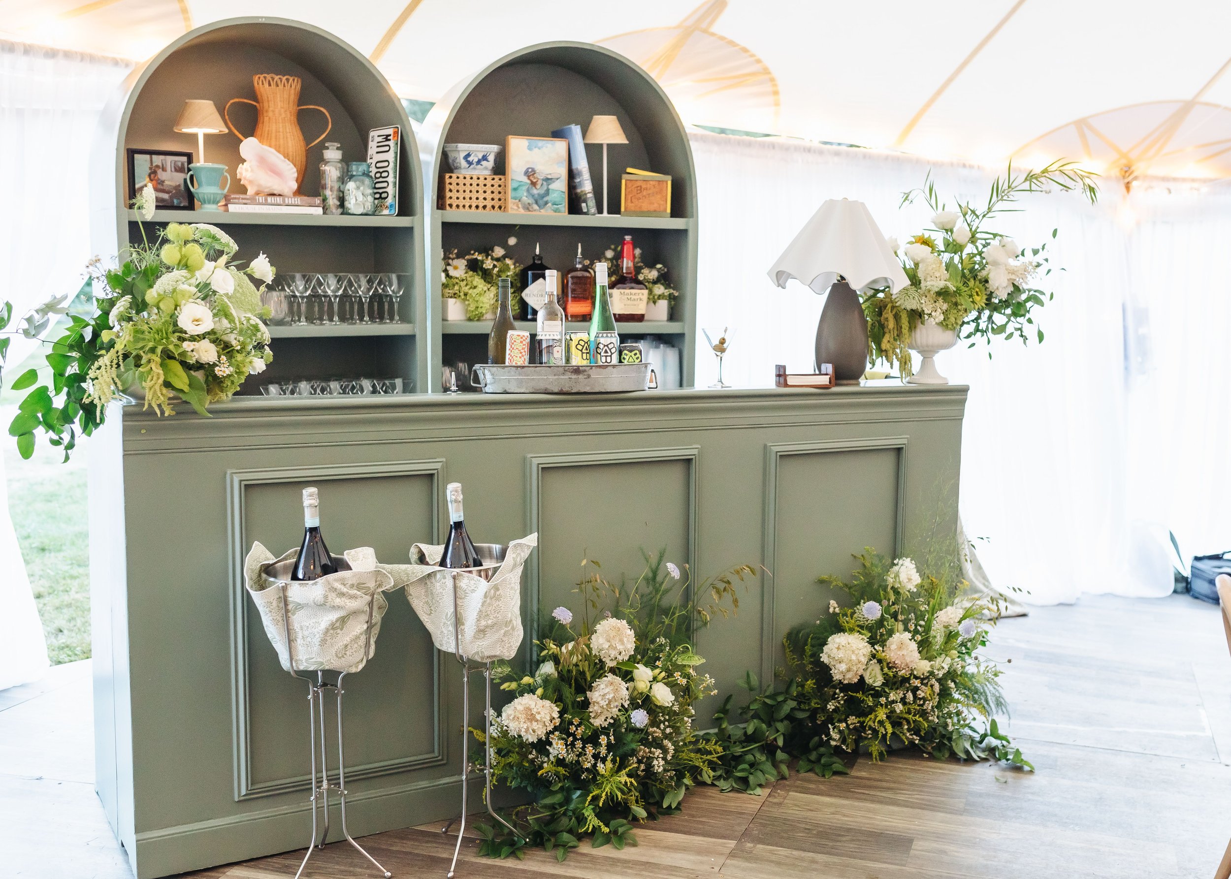 Decorative bar area with gray cabinets, white flower arrangements, and glassware in a bright indoor or outdoor setting.