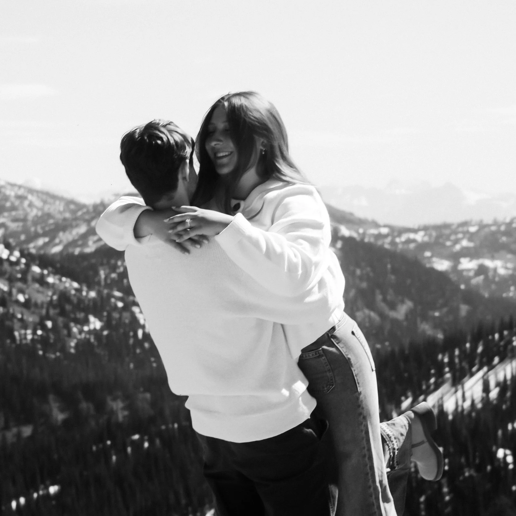 A couple in a loving embrace outdoors with mountains in the background.