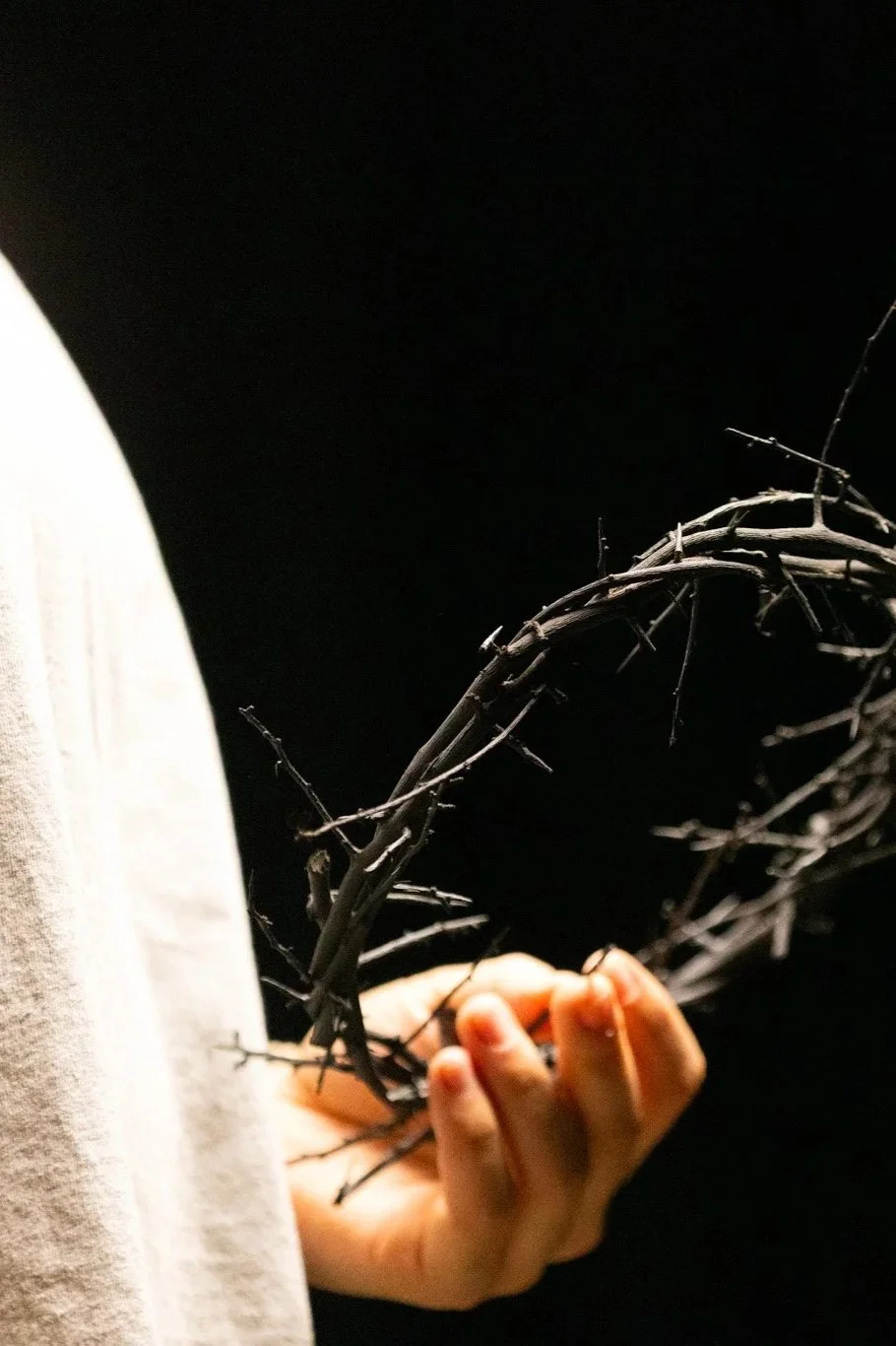 A person holding a circle made of intertwined, bare, thorny branches against a dark background.