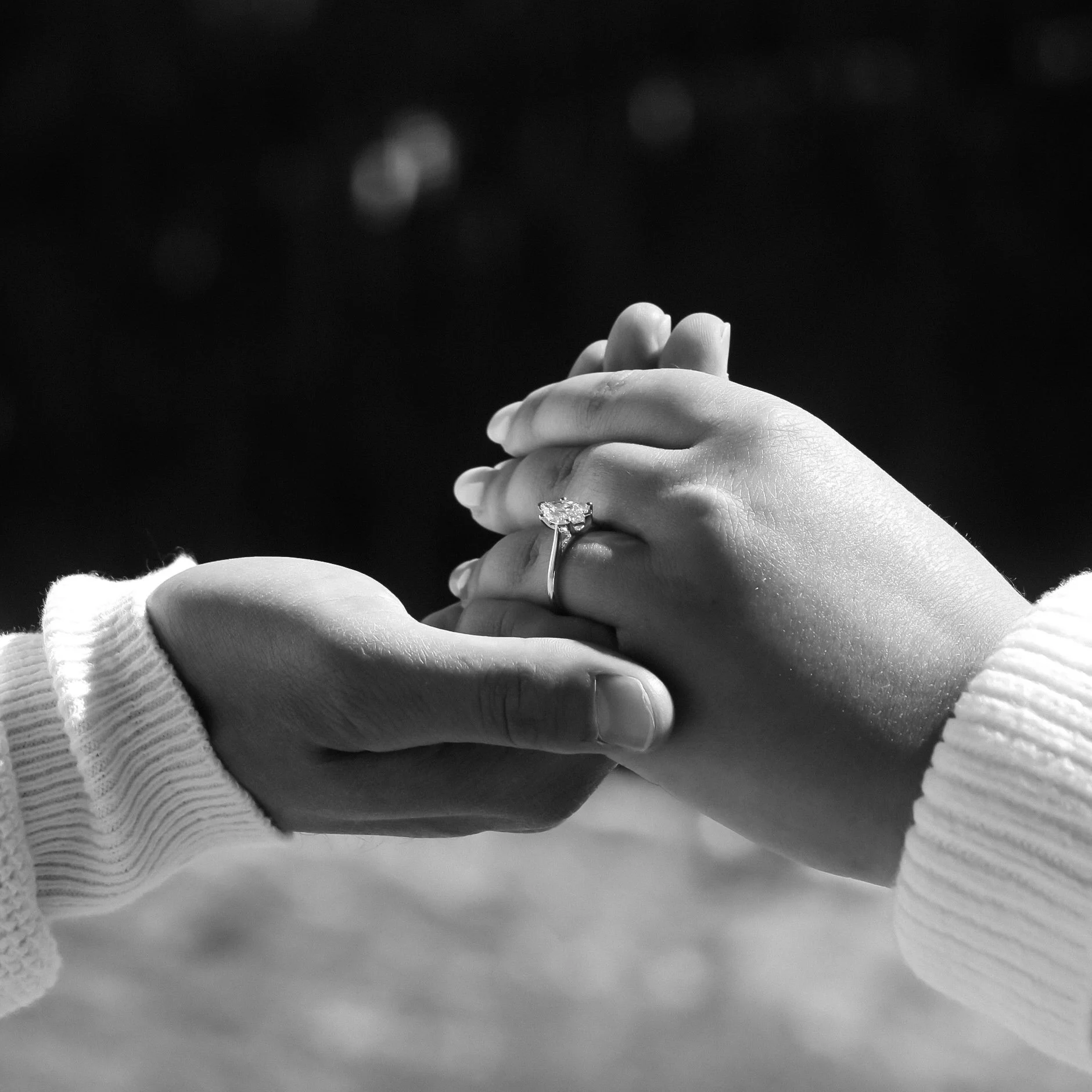 Close-up of a hand wearing a ring with a large gemstone, resting on a surface with a person's arm in a striped sleeve in the foreground.