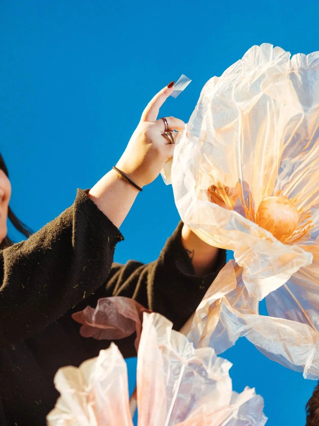 Close-up of a person holding a string with a paper lantern or decoration, against a clear blue sky.