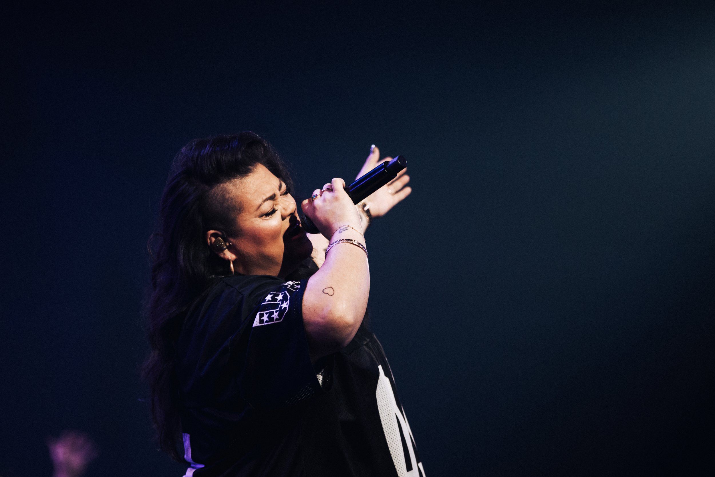 Female singer performs passionately on stage, holding a microphone with her eyes closed and expressive gestures.