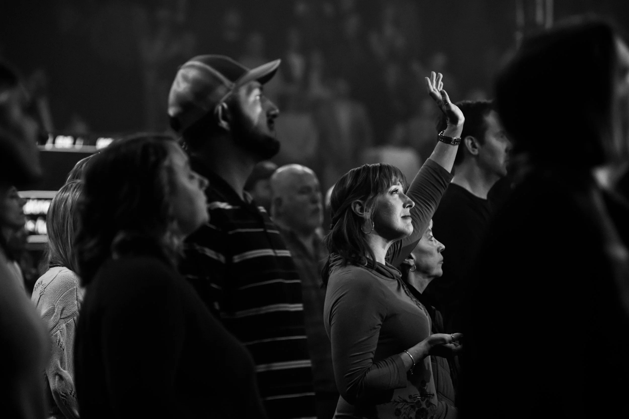 A group of people attending an event, with one woman raising her hand. The image is in black and white, showing diverse individuals seated and attentive.