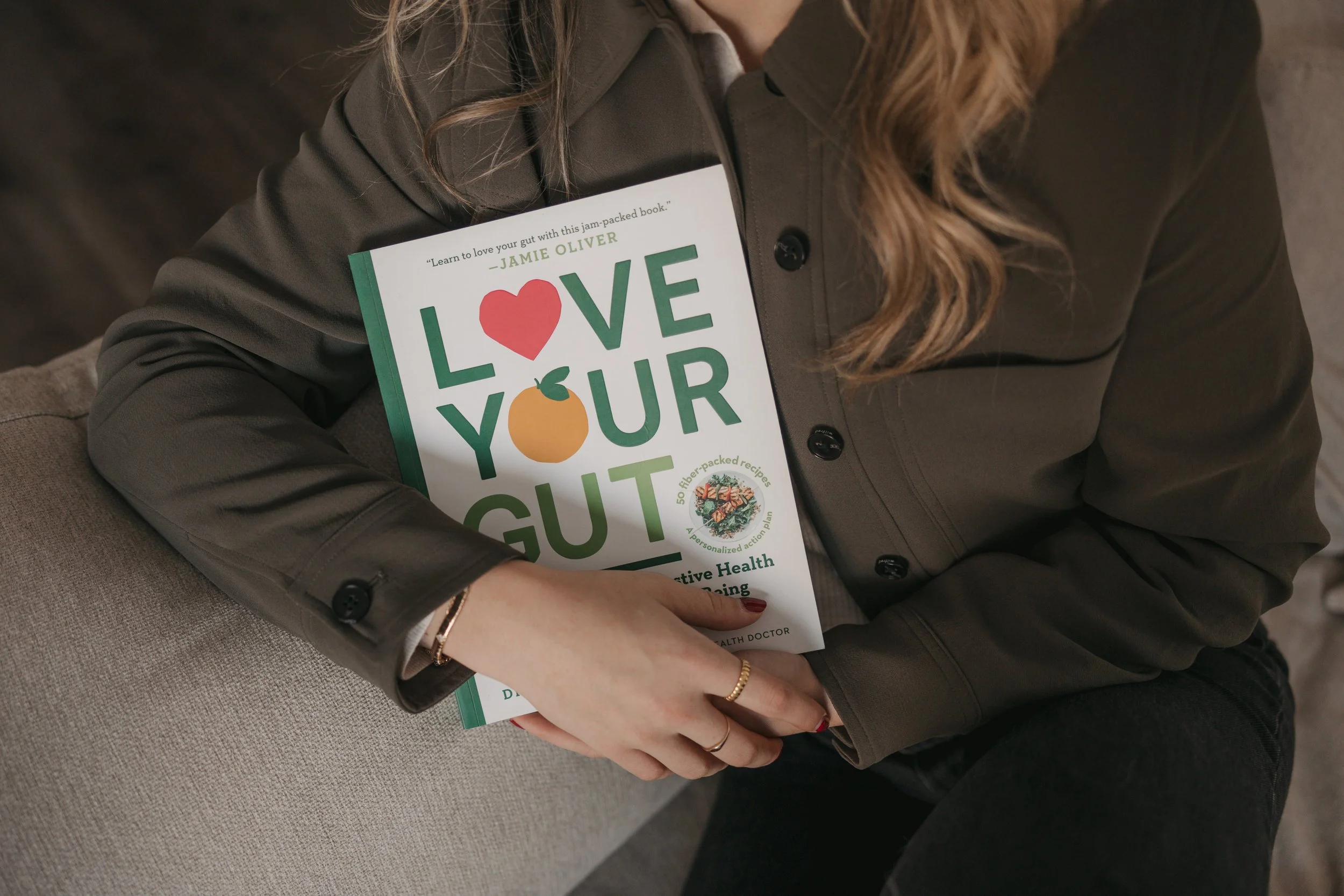 Person wearing a gray jacket holding a cookbook titled 'Love Your Gut'.
