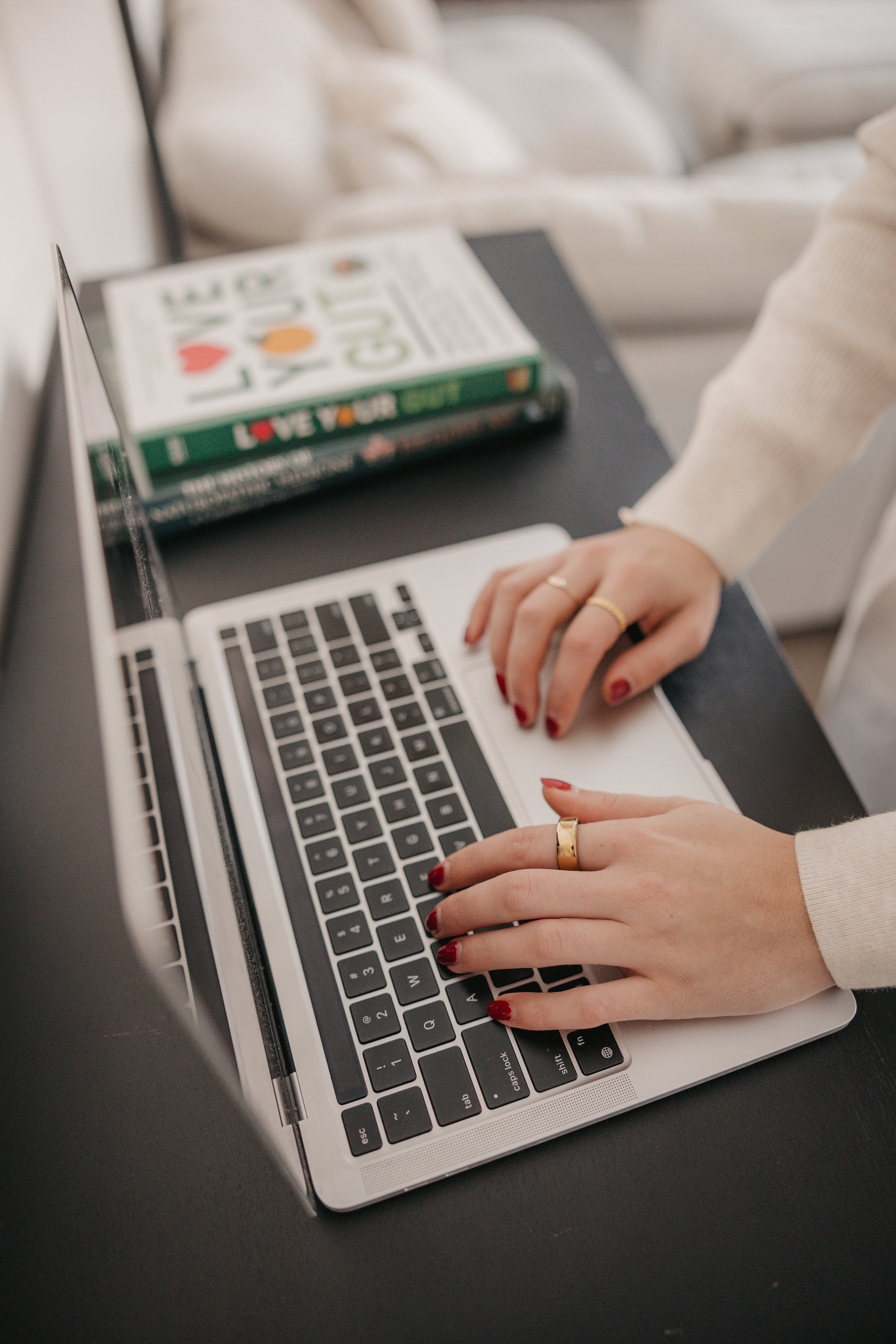 Person typing on a laptop with a book titled 'Love Your GF' on the desk.