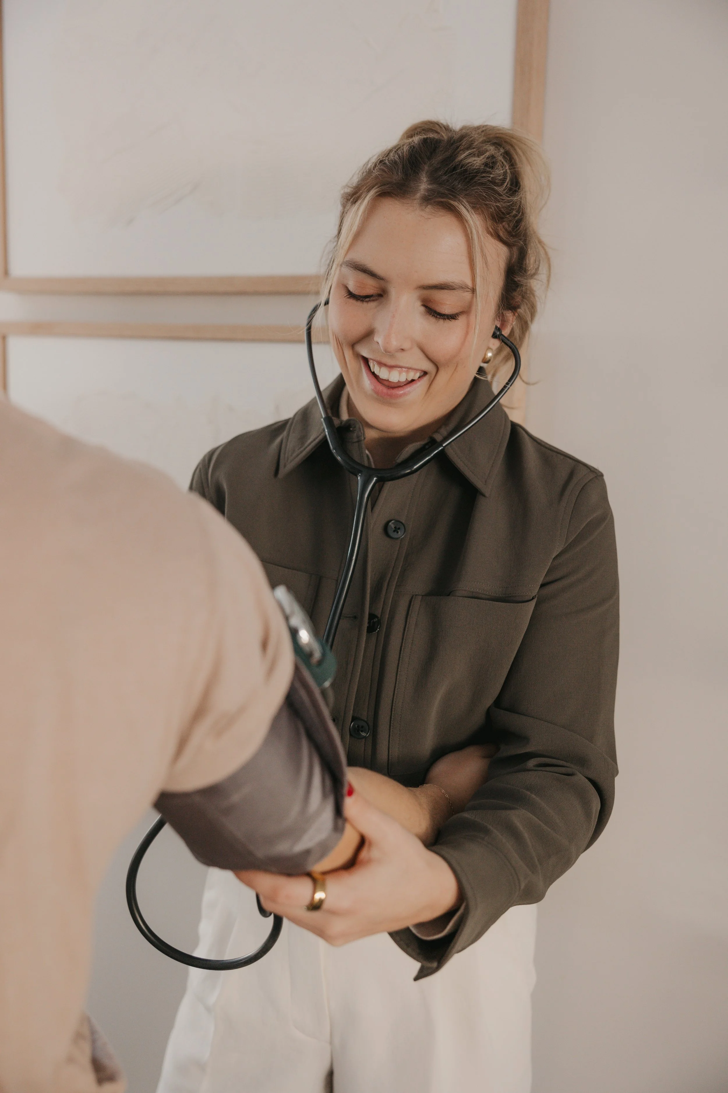 A female healthcare professional with a stethoscope around her neck is smiling and holding the arm of a patient, who appears to be undergoing a medical examination.