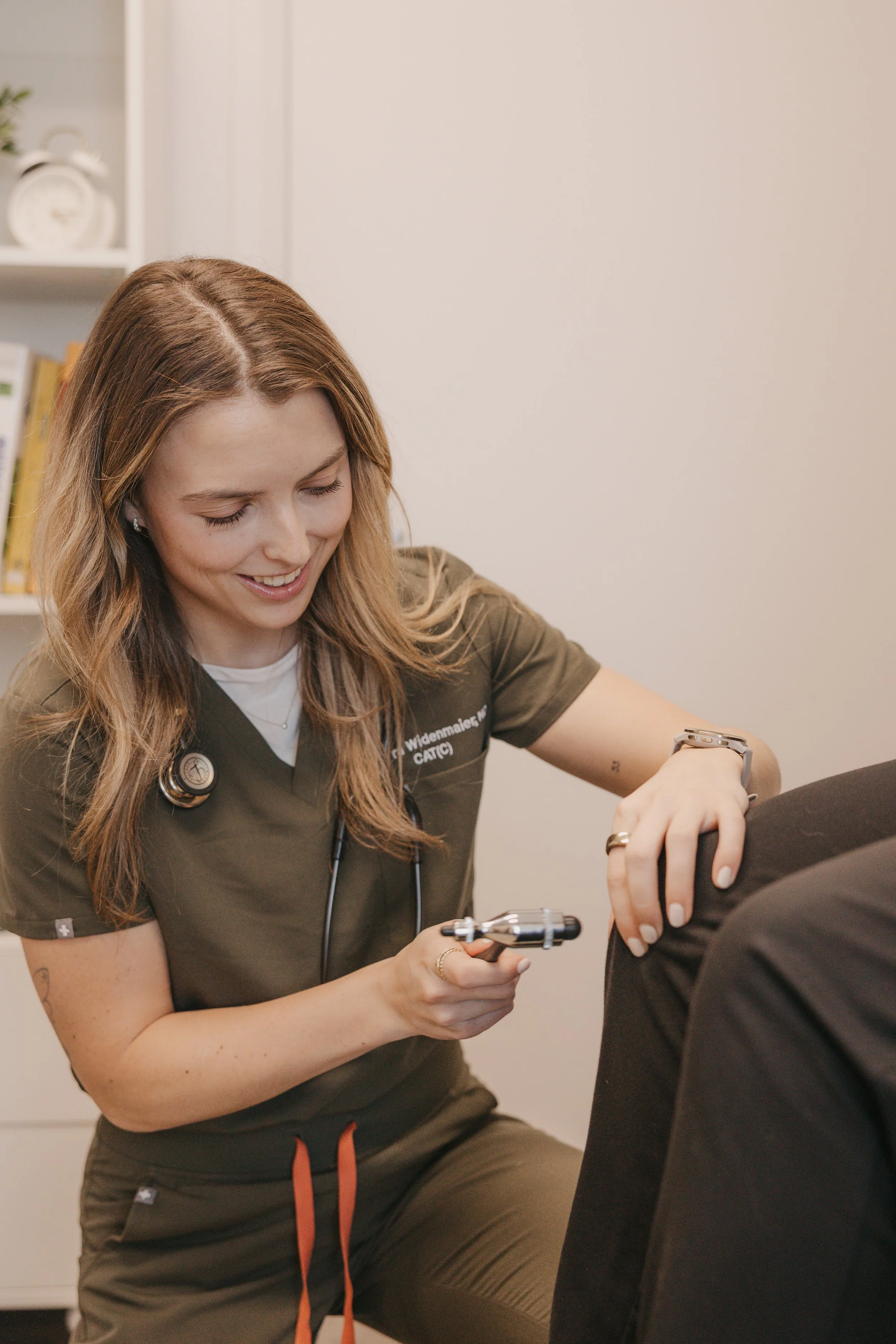 A female healthcare professional in scrubs assisting a patient with a blood pressure cuff.