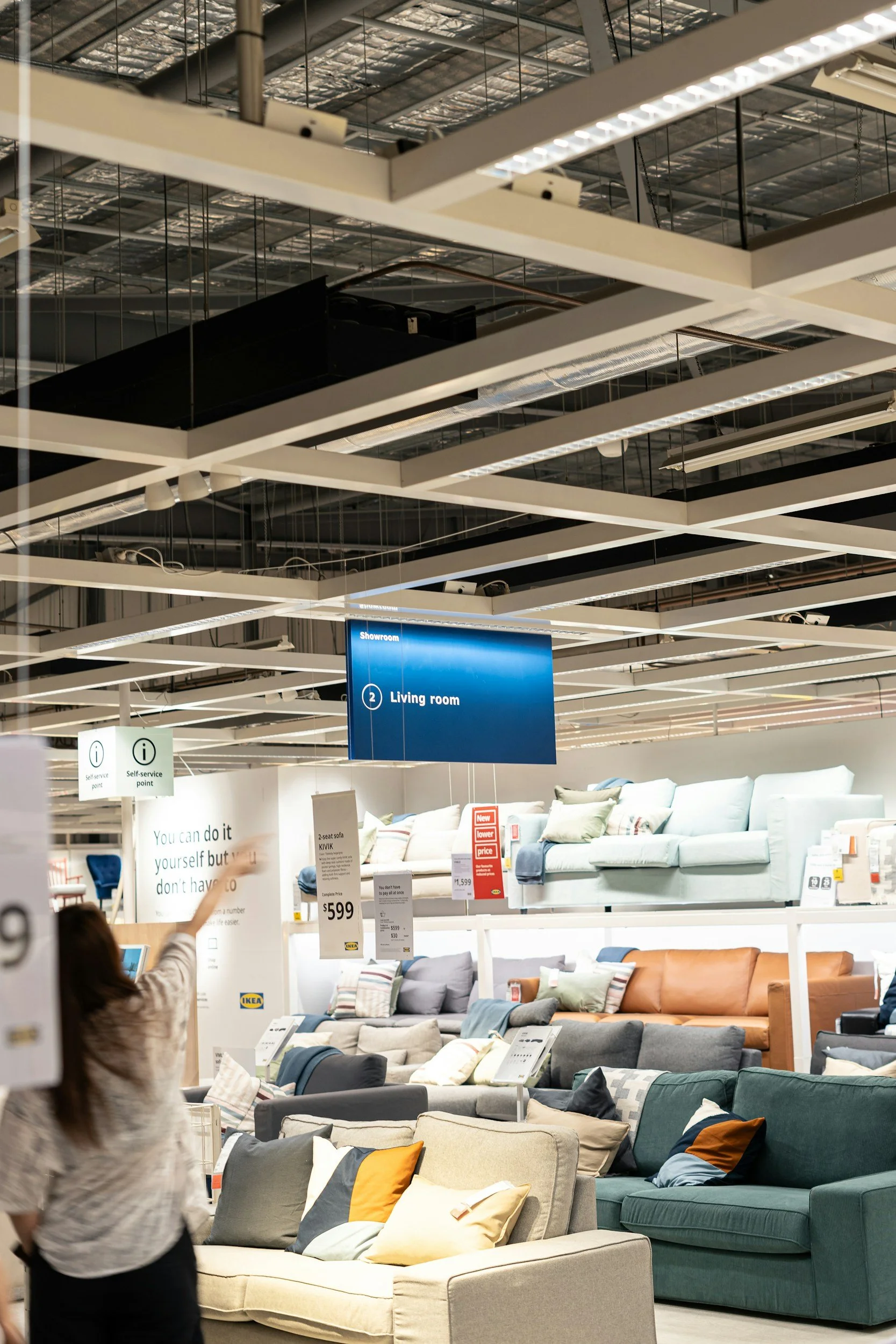 A furniture store display with sofas and cushions in various colors, with overhead lighting and sale signs, and a blue sign indicating the living room area.