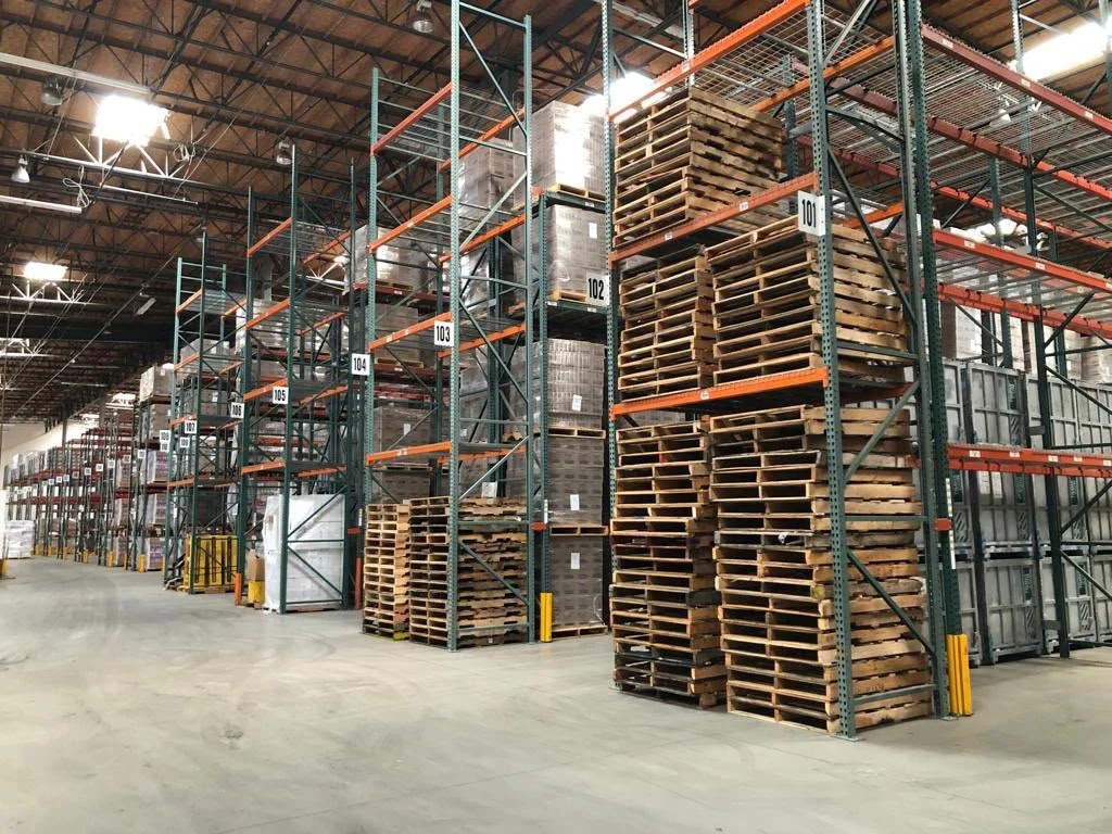Empty warehouse with tall metal shelving filled with wooden pallets and crates.