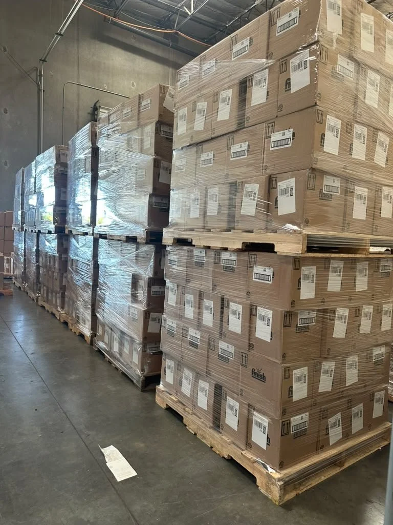 Stacked pallets of boxed items wrapped in plastic in a warehouse.