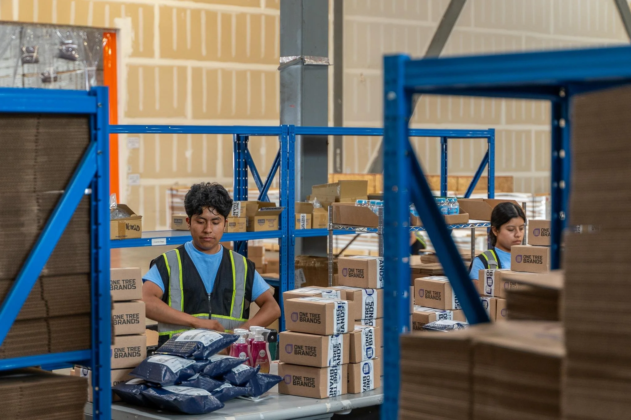 Warehouse workers organizing boxes on shelves, some children watching, industrial setting with high ceilings and storage racks.