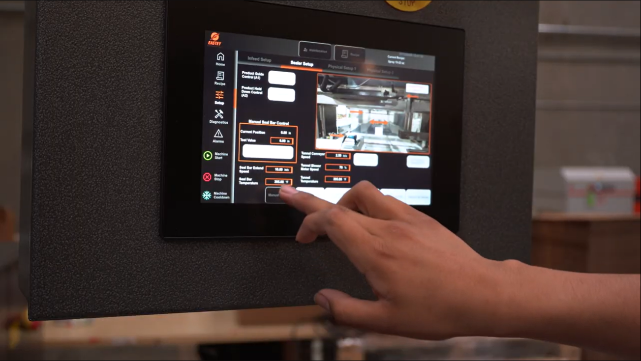 Close-up of a person's hand interacting with a touchscreen control panel on a machine, displaying settings and a small image of the machine's interior.
