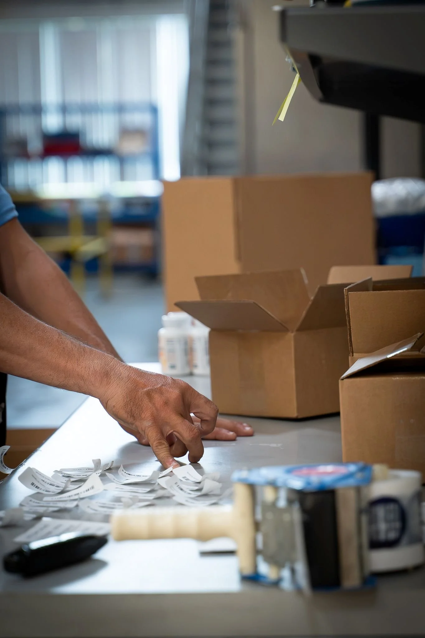 Person sorting paper receipts on a table next to open cardboard boxes, with various supplies in the background.