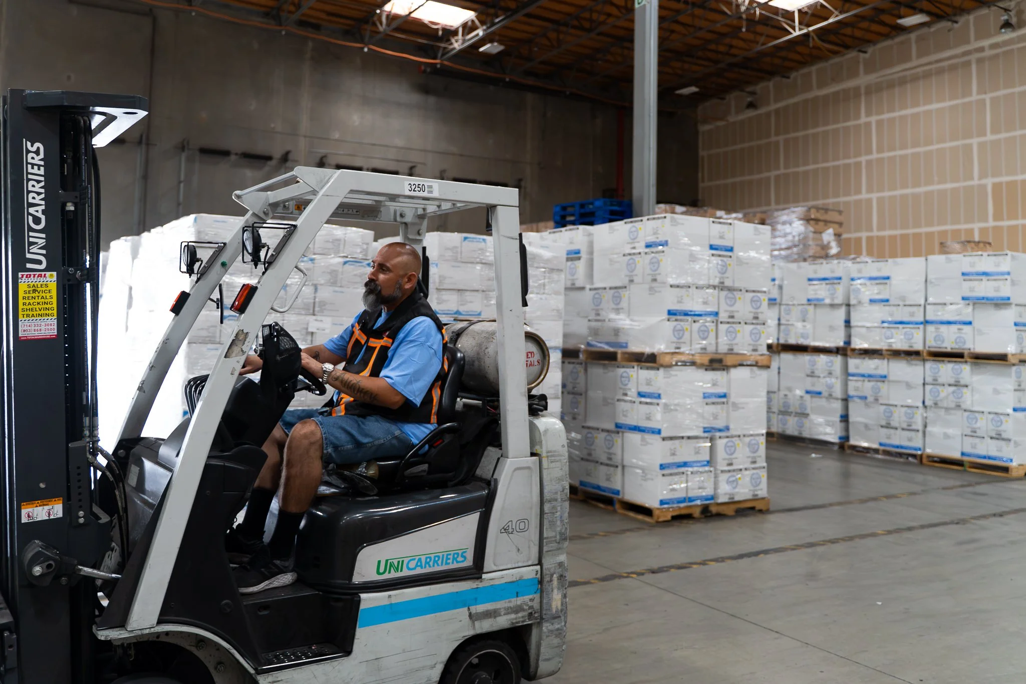 A man operating a forklift in a warehouse with stacked boxes on pallets.