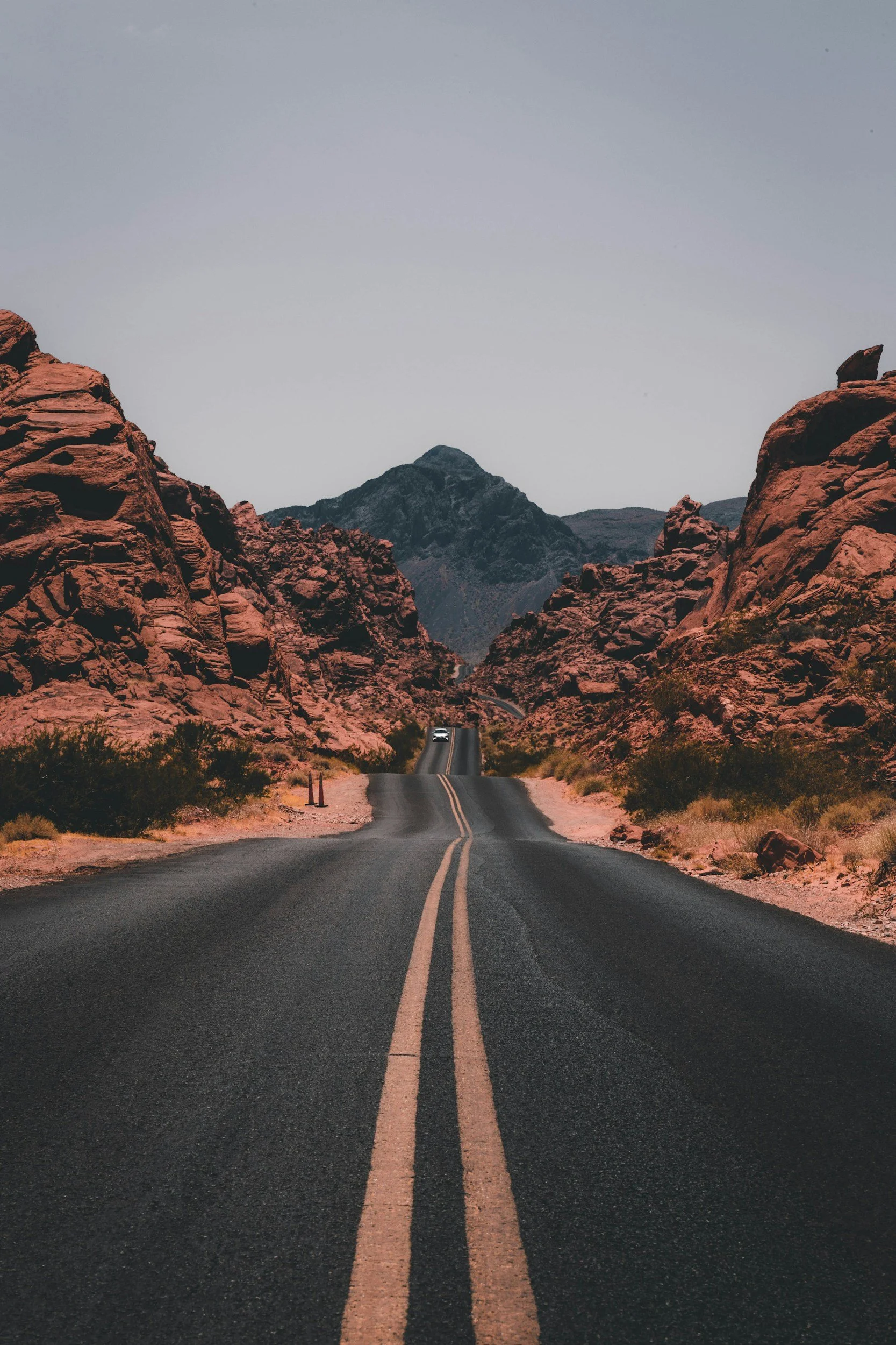 A long straight road runs through a desert canyon with reddish rock formations on either side, leading toward distant mountains under a clear sky.