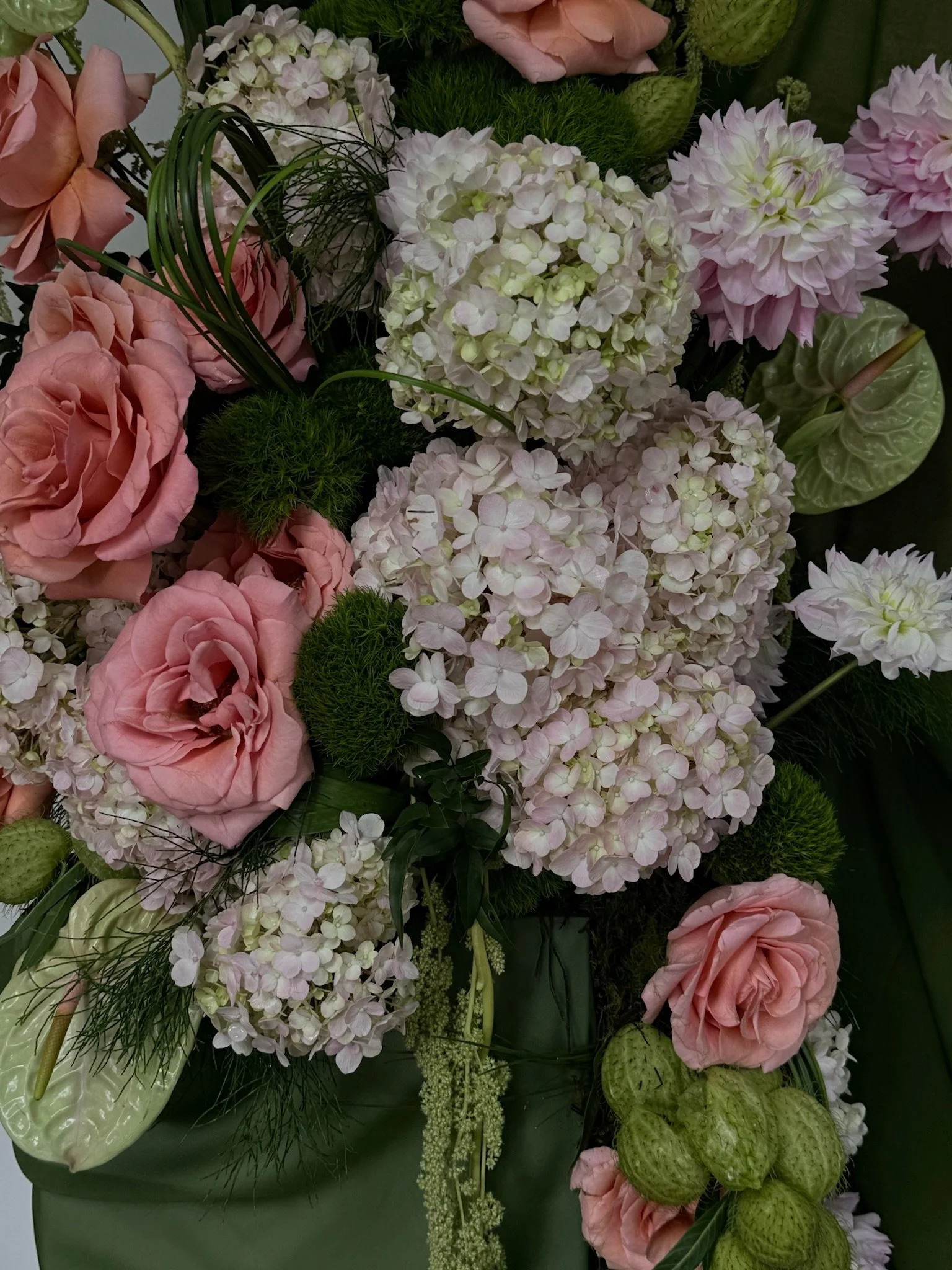 A floral arrangement featuring pink roses, white hydrangeas, pink dahlias, green anthuriums, and various greenery.